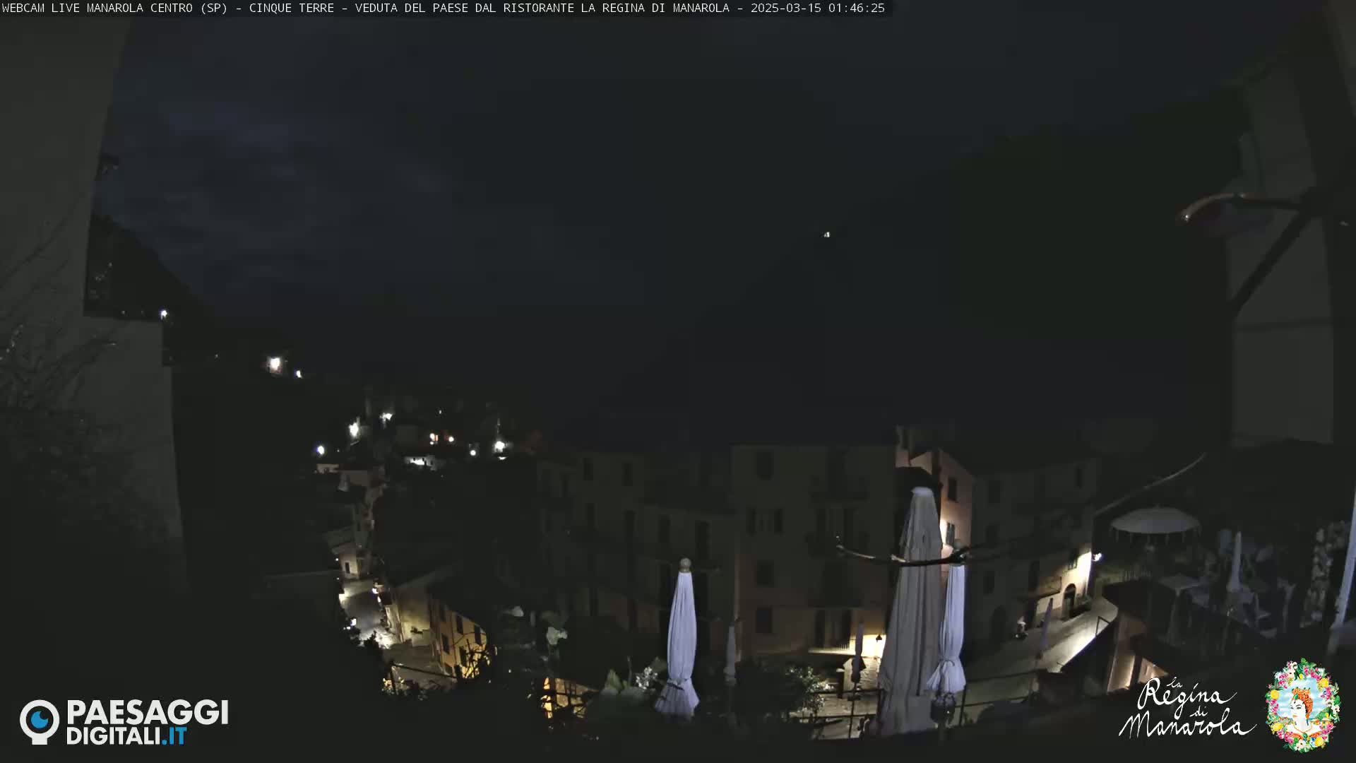 A nighttime, dimly lit view of a town nestled on a hillside, with several closed umbrellas visible in the foreground.