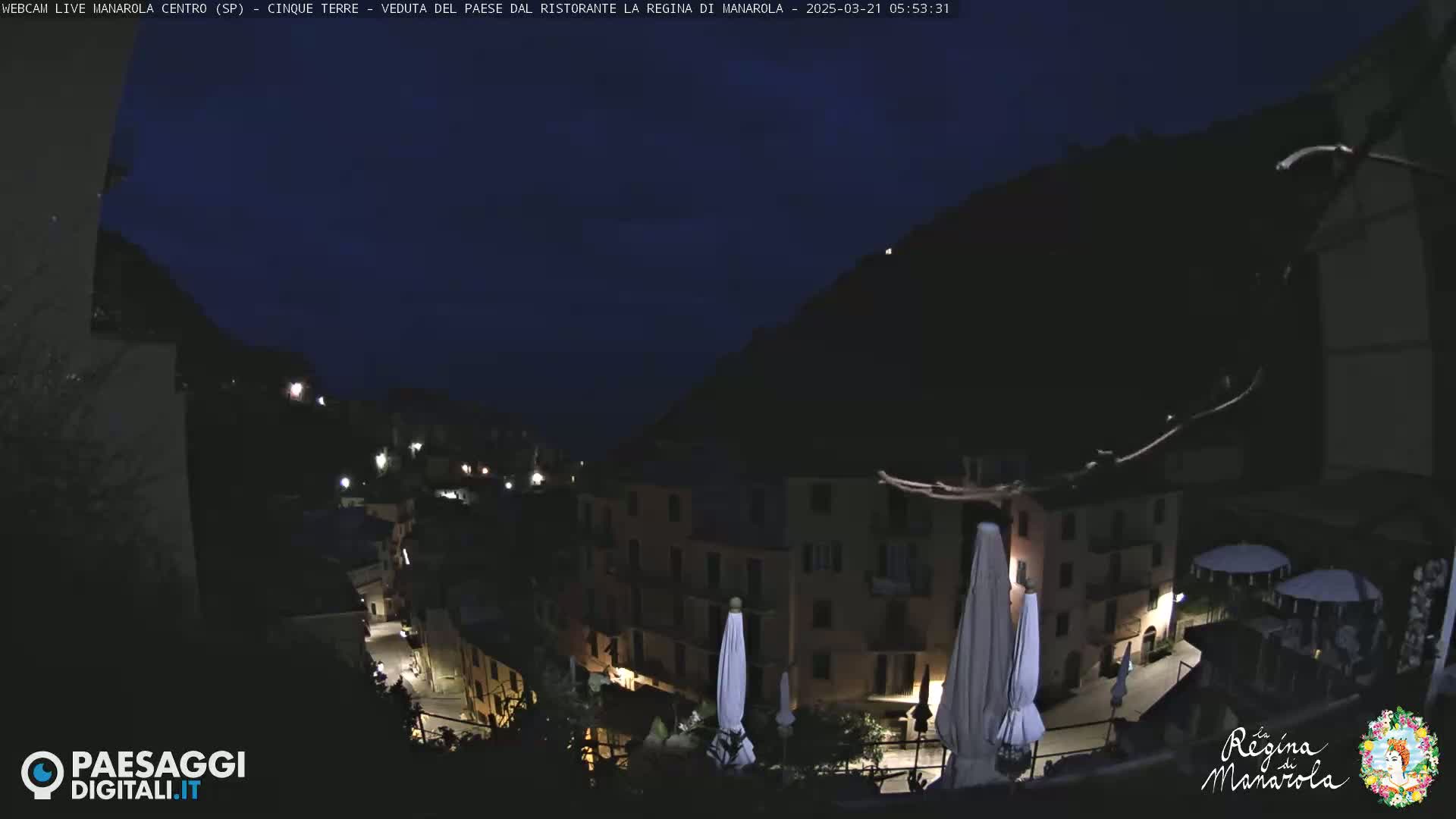 A nighttime view of a dimly lit village nestled into a hillside, under a dark blue sky.