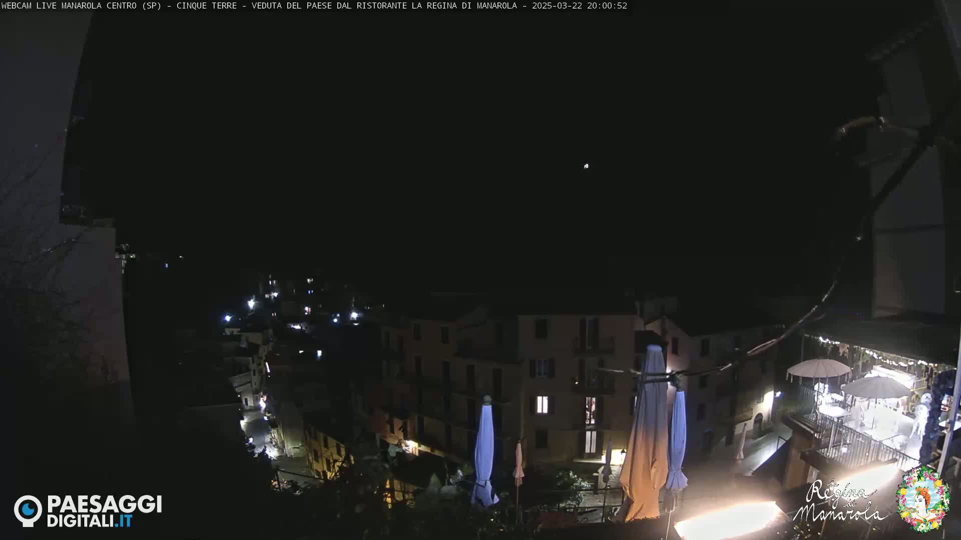 A nighttime, high-angle view of a village nestled on a hillside, with several lights illuminating the buildings and streets.