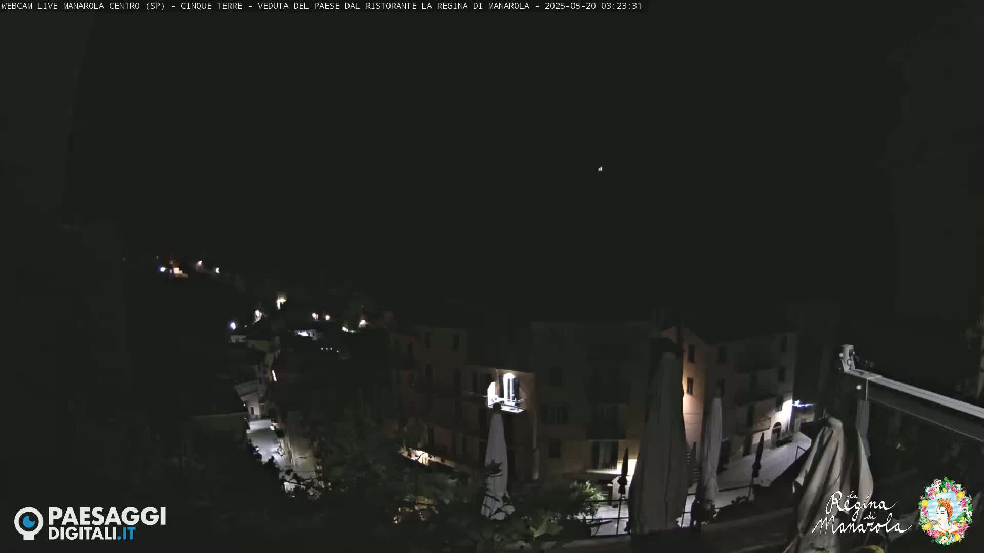 A nighttime view of a small, illuminated town nestled on a hillside under a clear, dark sky.