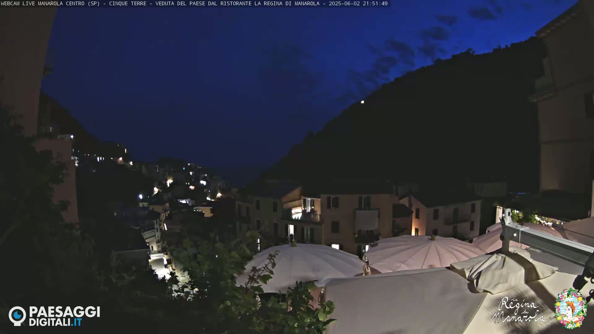 A nighttime view of a hillside town illuminated with lights, under a dark blue, mostly clear sky.
