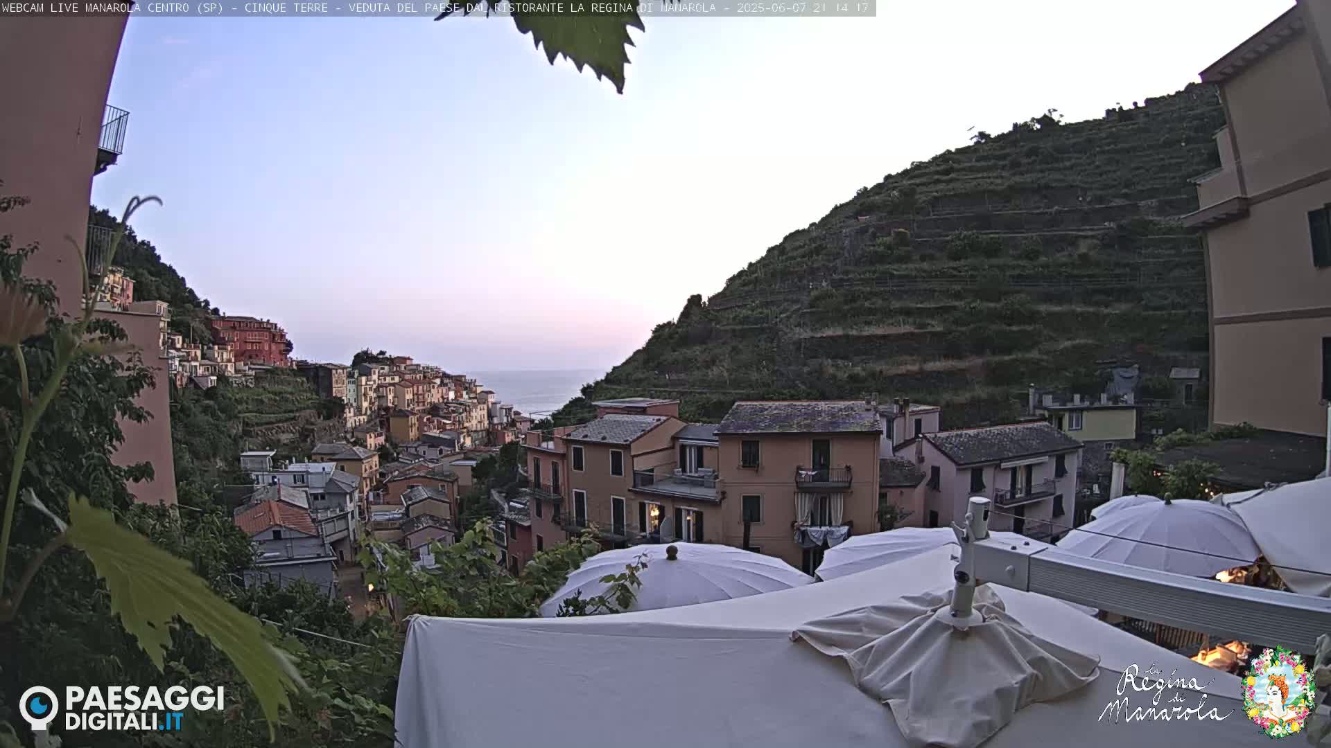 A hillside village with colorful buildings overlooks the ocean under a twilight sky.