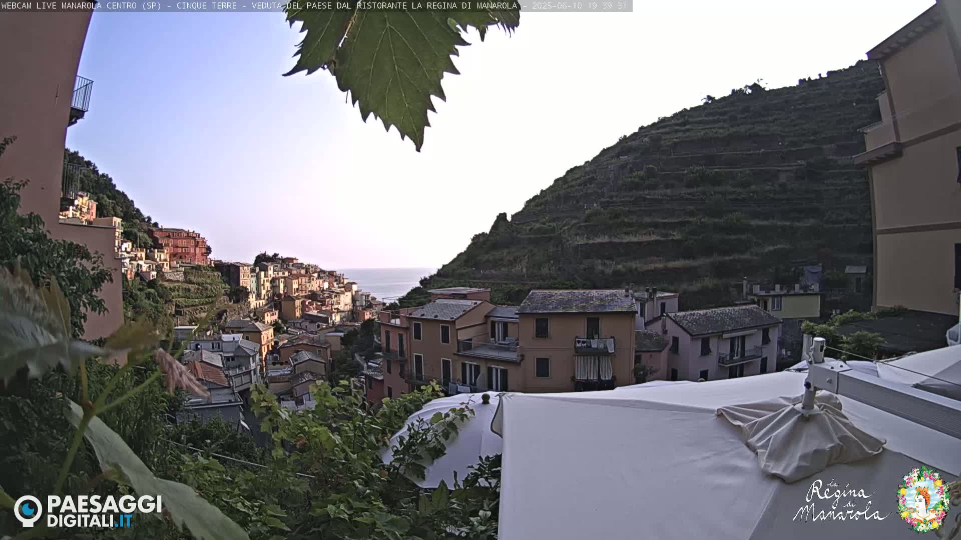 A hillside village of colorful buildings overlooks the ocean under a mostly clear sky.