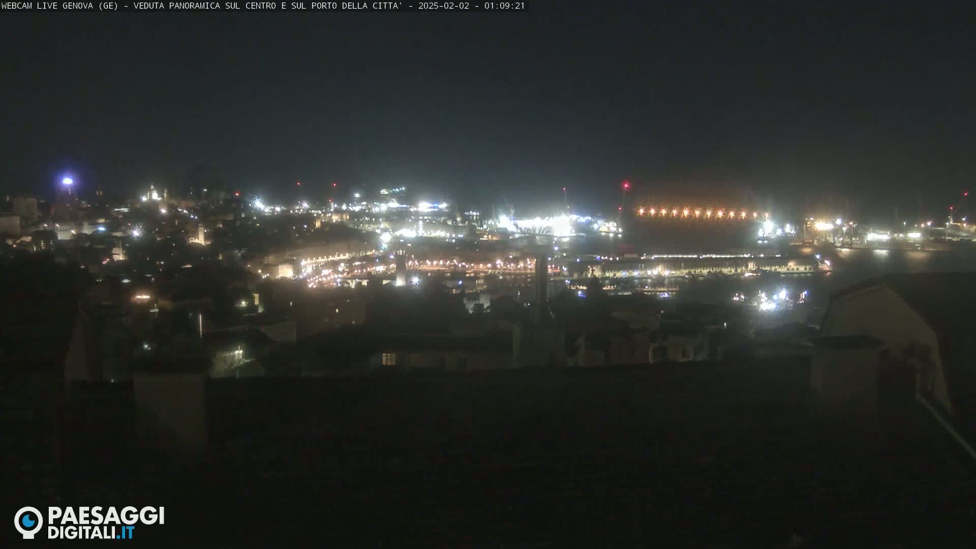 A nighttime, panoramic view of a city's illuminated harbor and buildings.