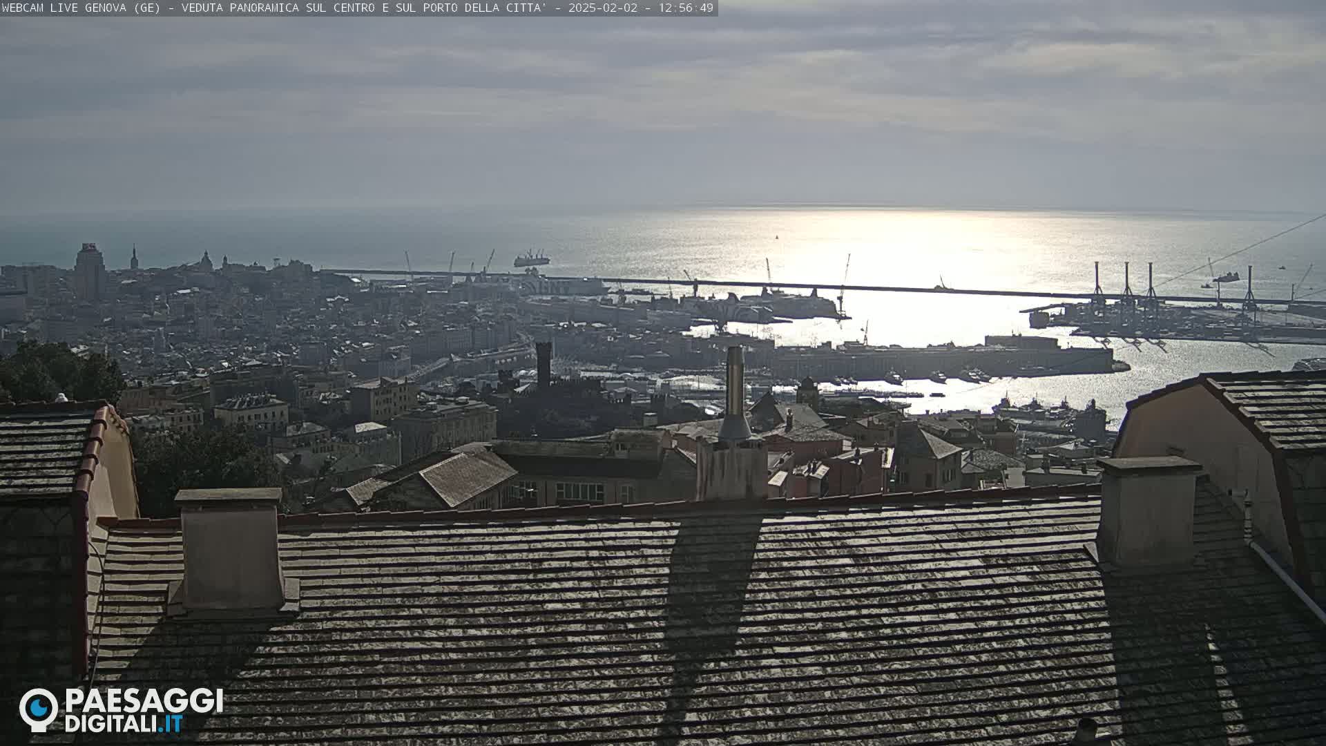 A panoramic view of a city and harbor on a sunny day, with the sun glinting off the water.