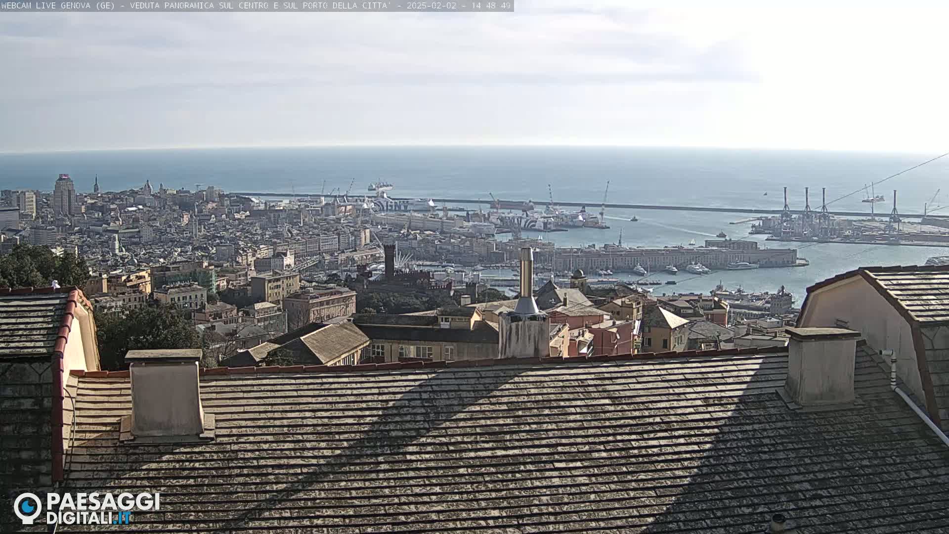 A panoramic view of a city and harbor on a sunny day, with the ocean visible in the distance.