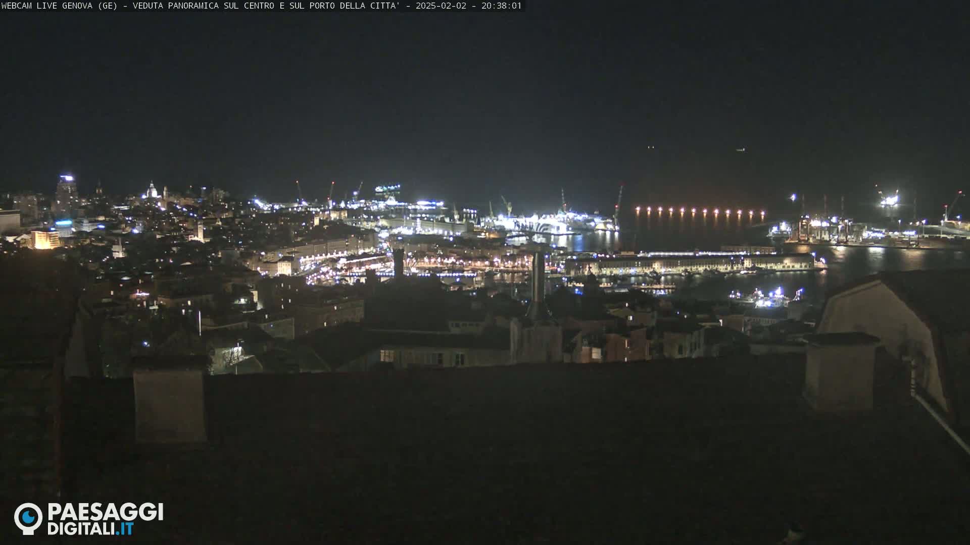 A nighttime, panoramic view of a city's illuminated harbor and buildings.