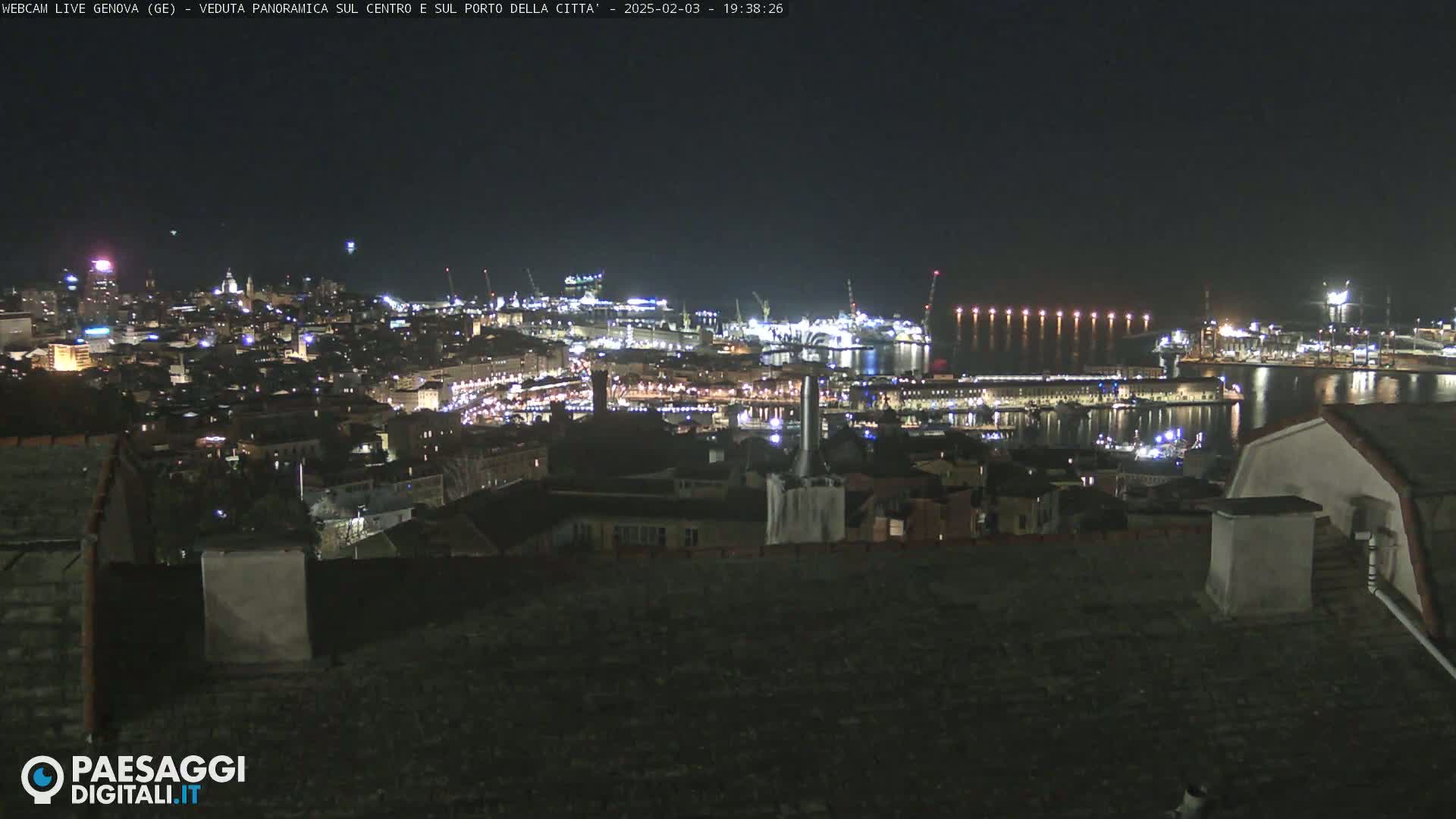 A nighttime panoramic view of a city harbor with many lights illuminating buildings and ships, under a clear sky.