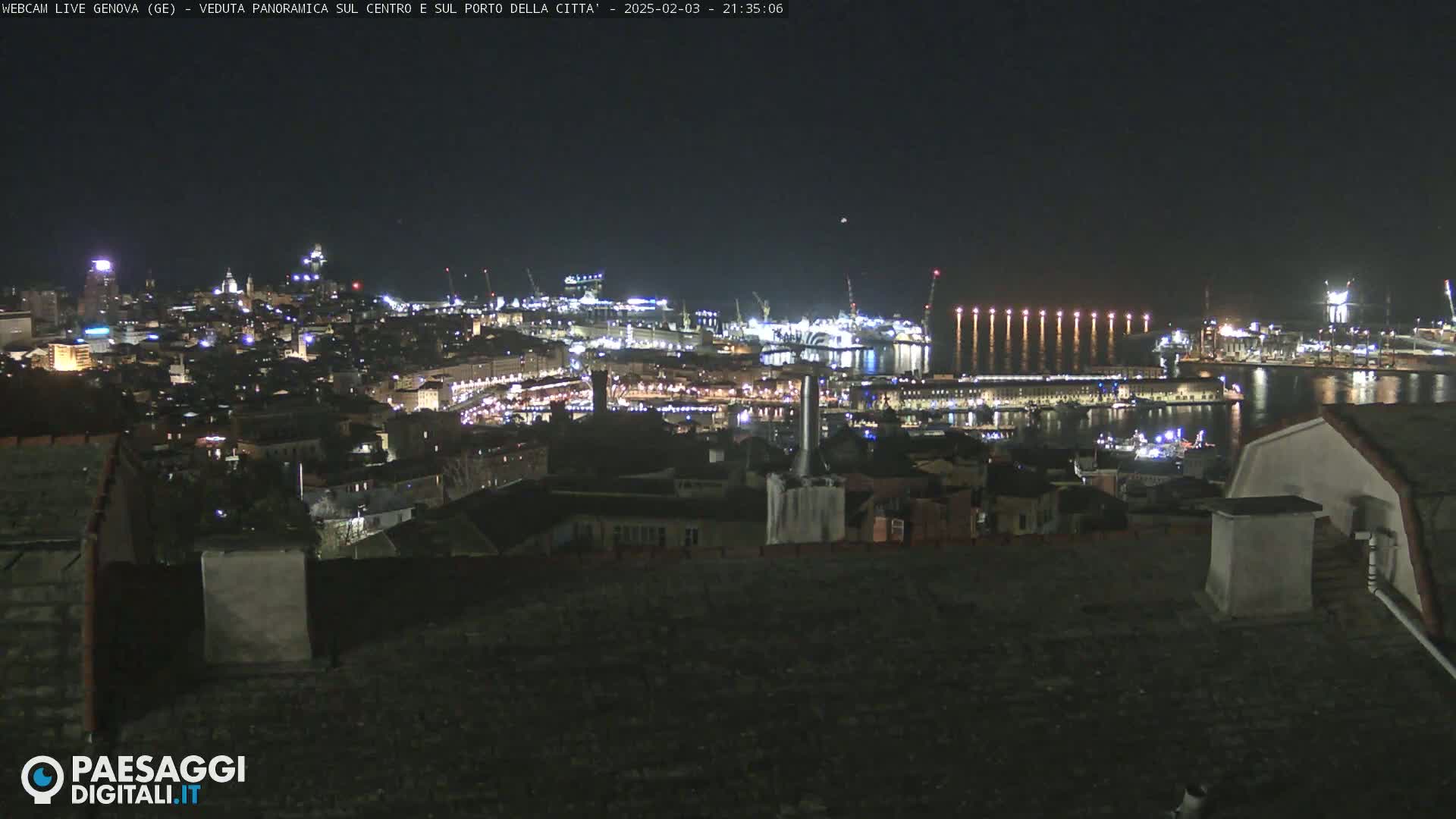 A nighttime, panoramic view of a city's harbor and illuminated cityscape, with calm water reflecting lights.