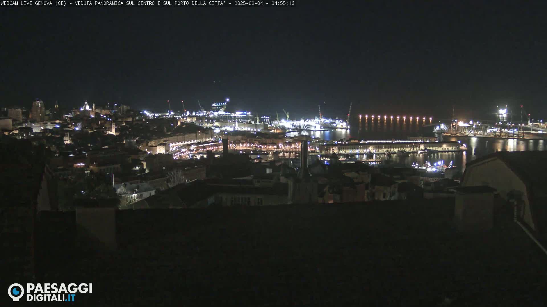 A nighttime panoramic view of a city and harbor illuminated by lights, under a clear, dark sky.