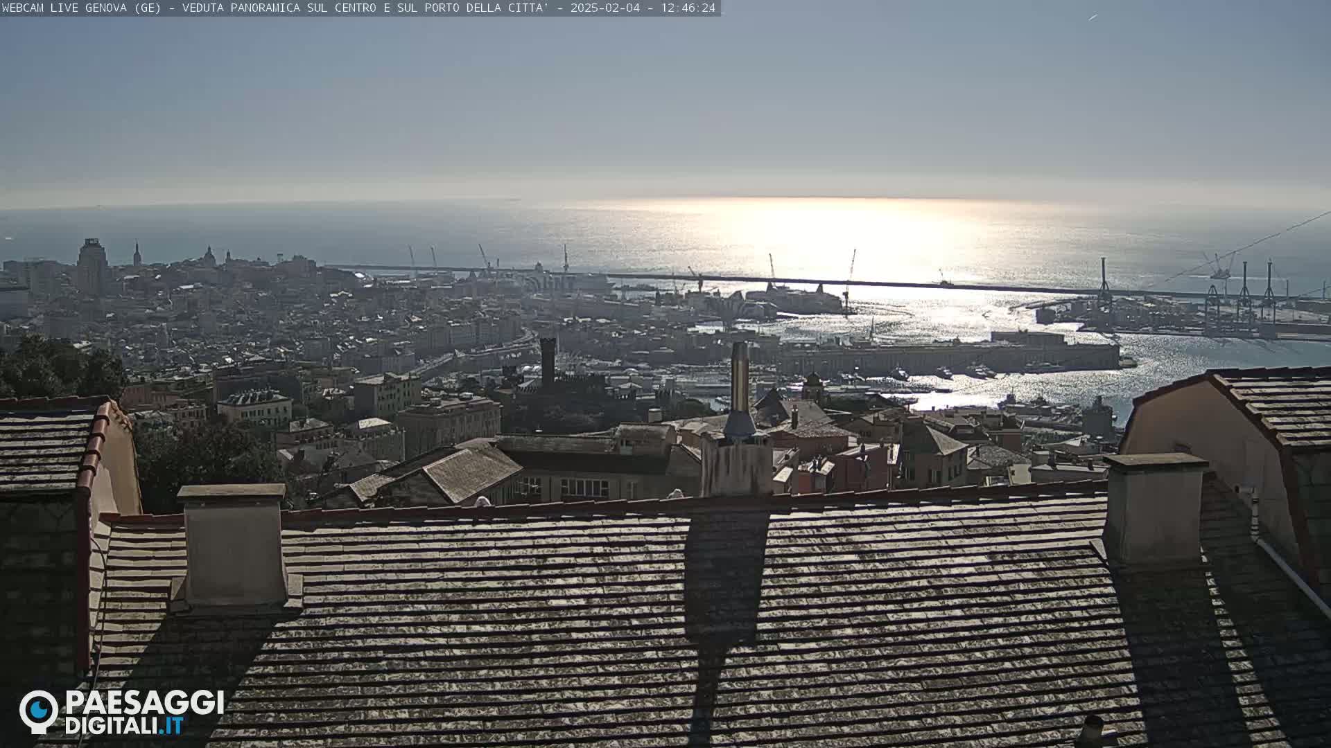 A panoramic view of a city and harbor, overlooking a calm sea reflecting sunlight under a clear sky.
