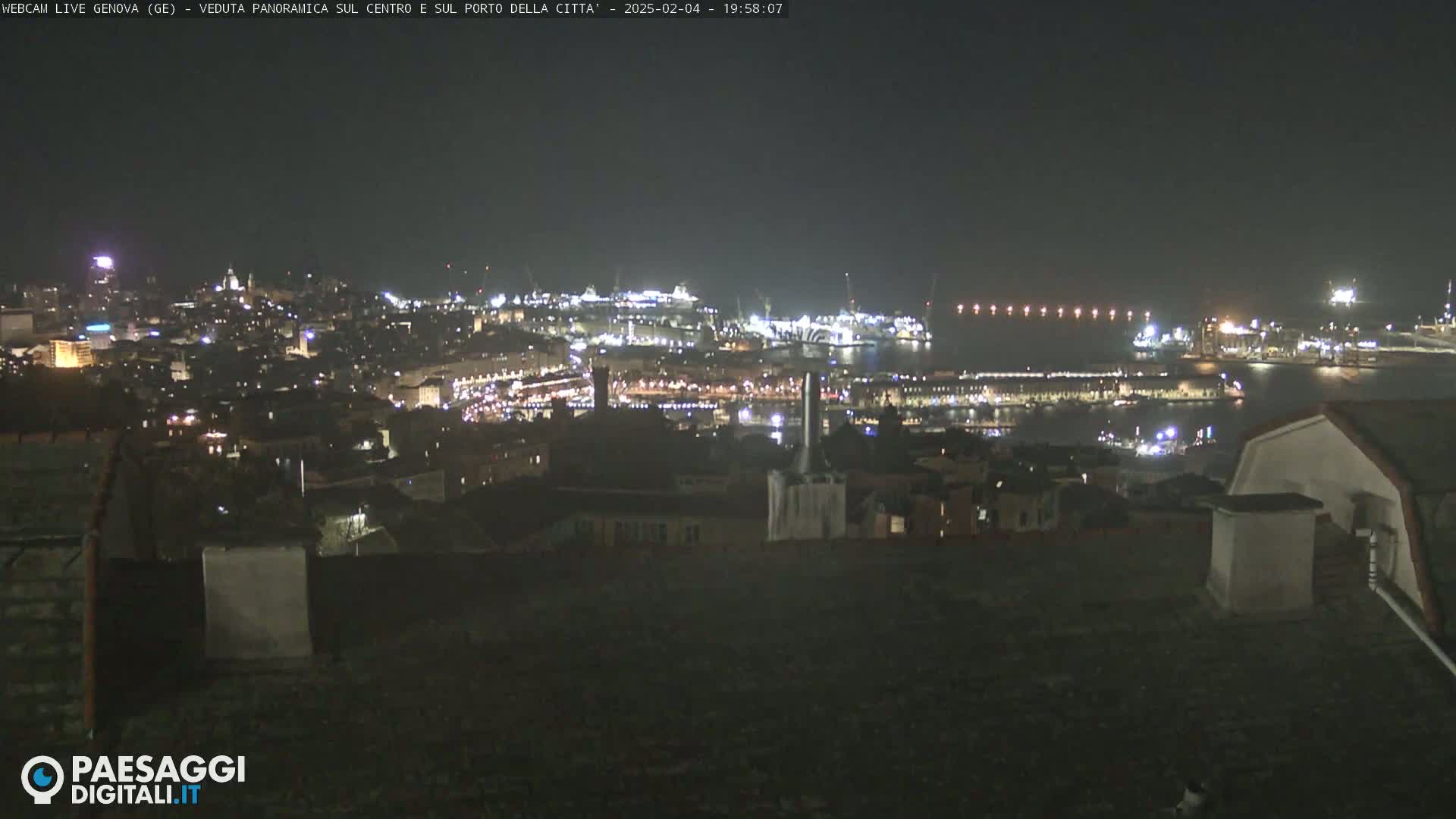 A nighttime panoramic view of a city and harbor, brightly lit against a dark sky.