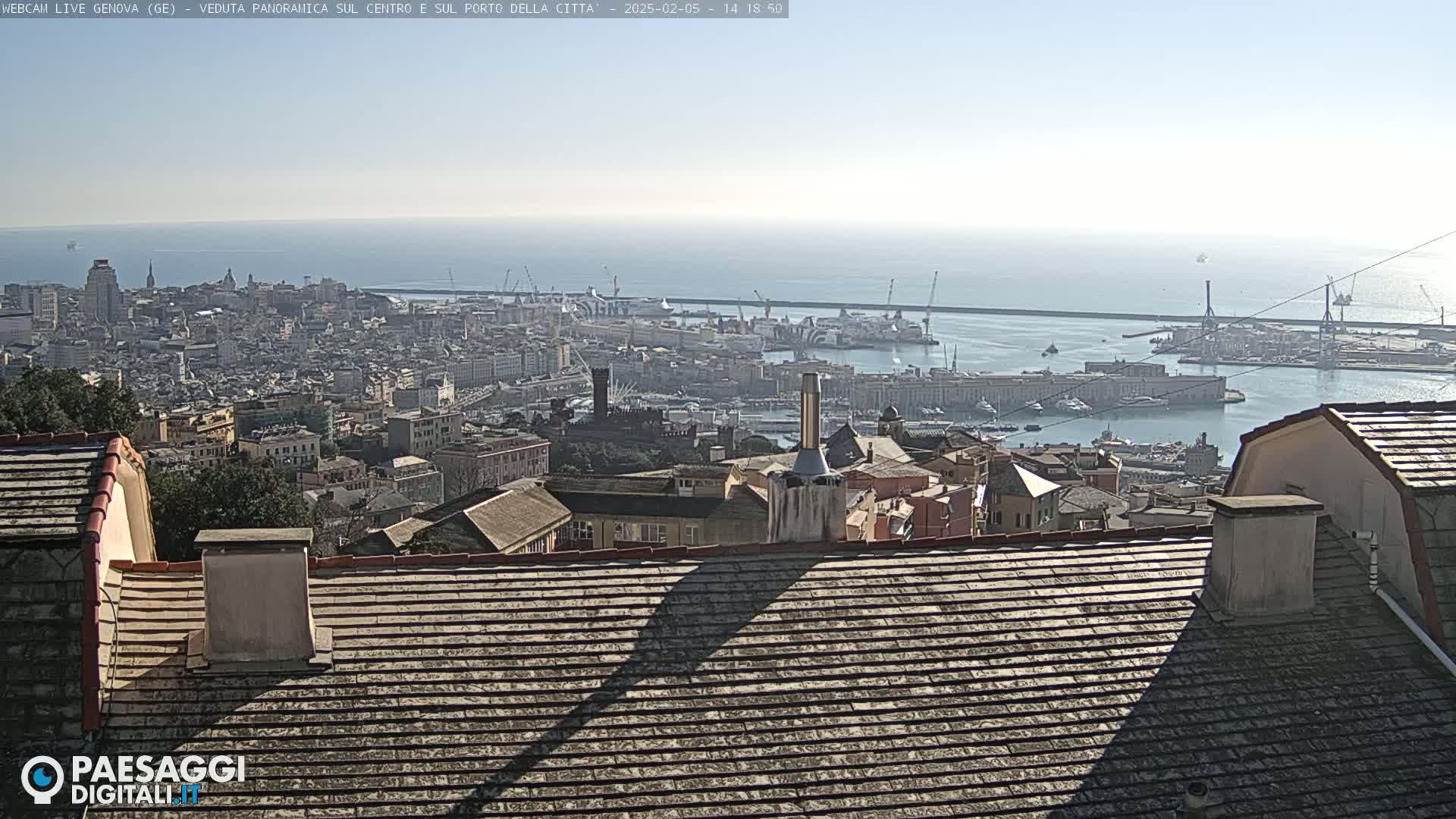 A panoramic view of a city and harbor on a sunny day, seen from a rooftop with tiled roofs.