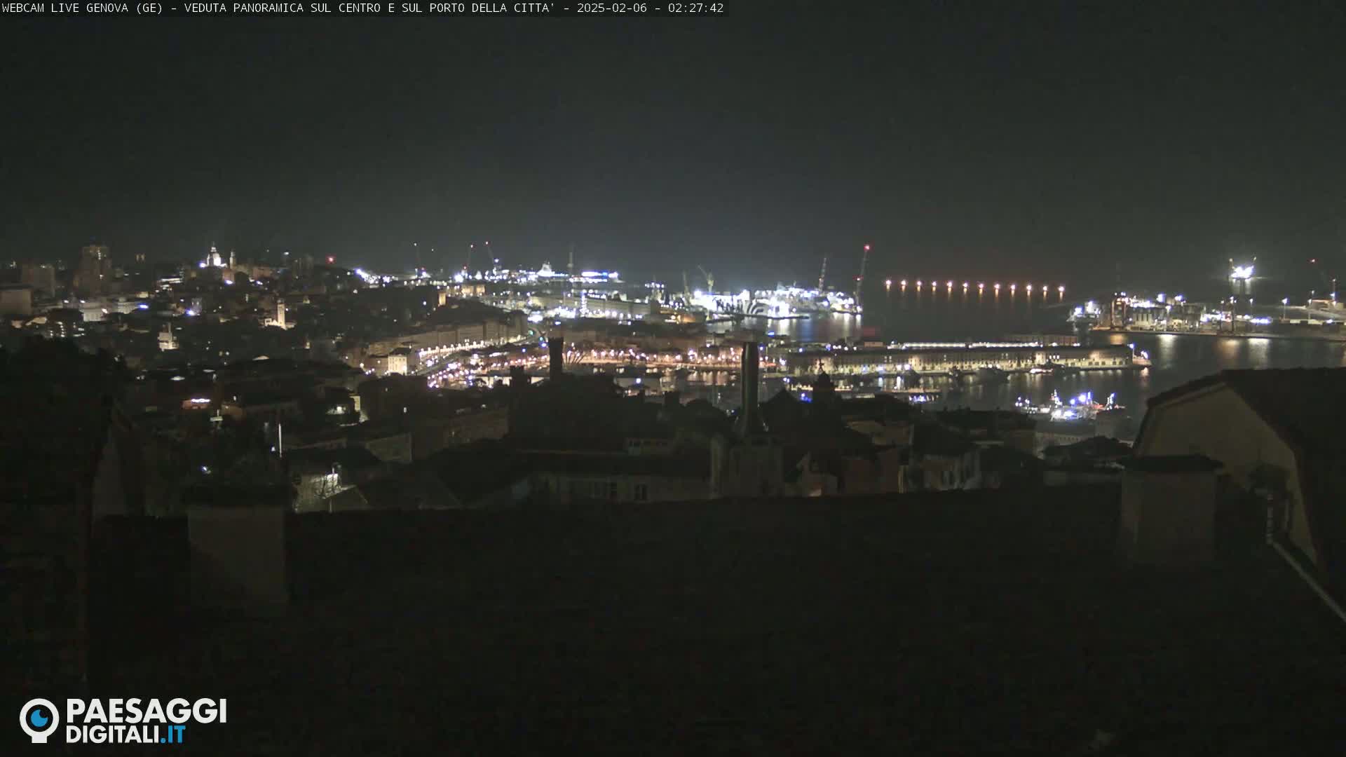 A nighttime panoramic view of a city's harbor and illuminated buildings, under a clear, dark sky.