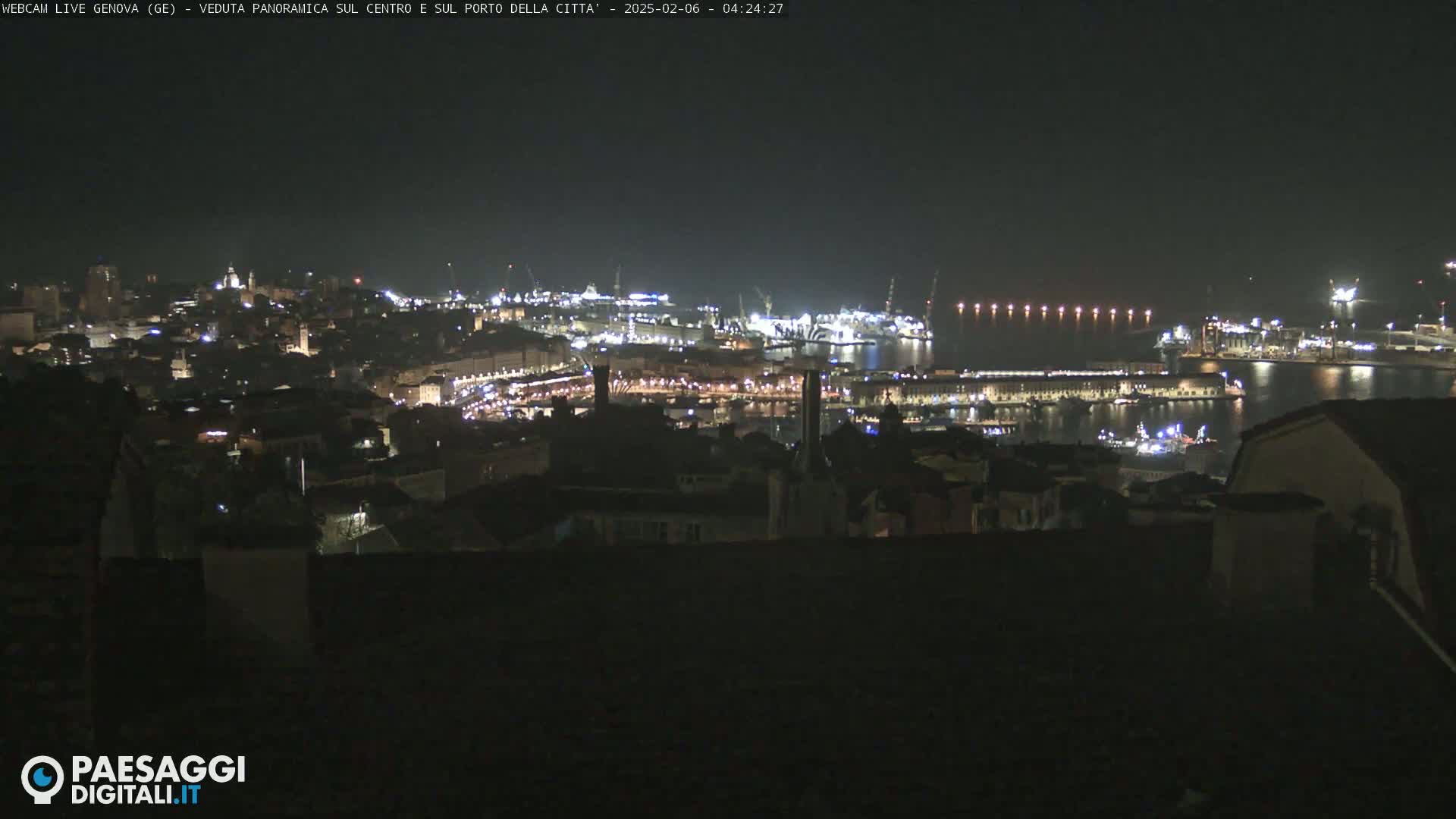 A nighttime, panoramic view of a city and harbor, illuminated by many lights.