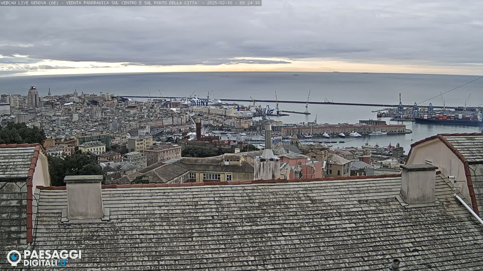 A panoramic view of a city and harbor on an overcast day shows a cityscape extending to a calm sea.