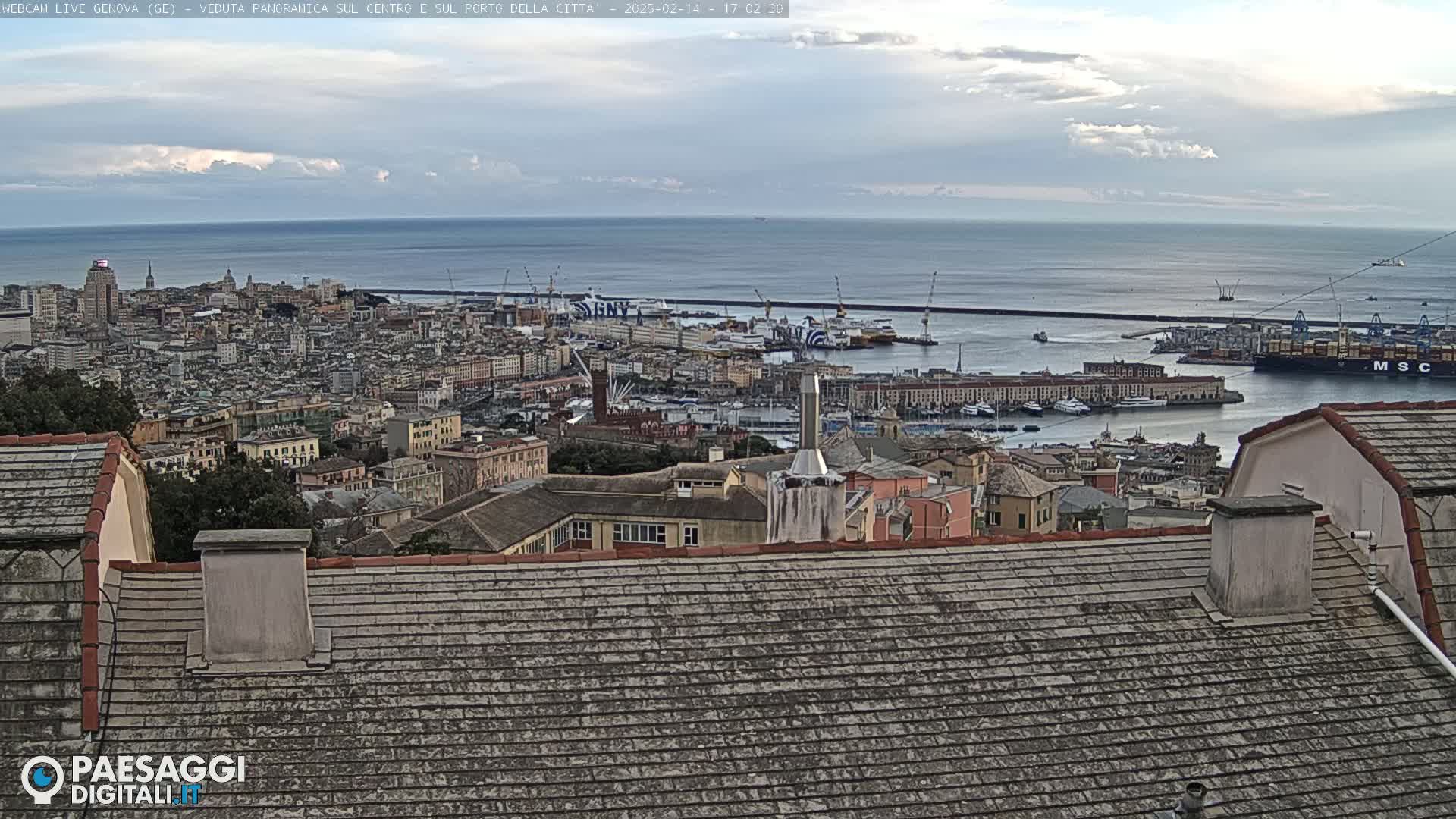 A panoramic view of a city and harbor, with a partly cloudy sky and calm sea in the background.