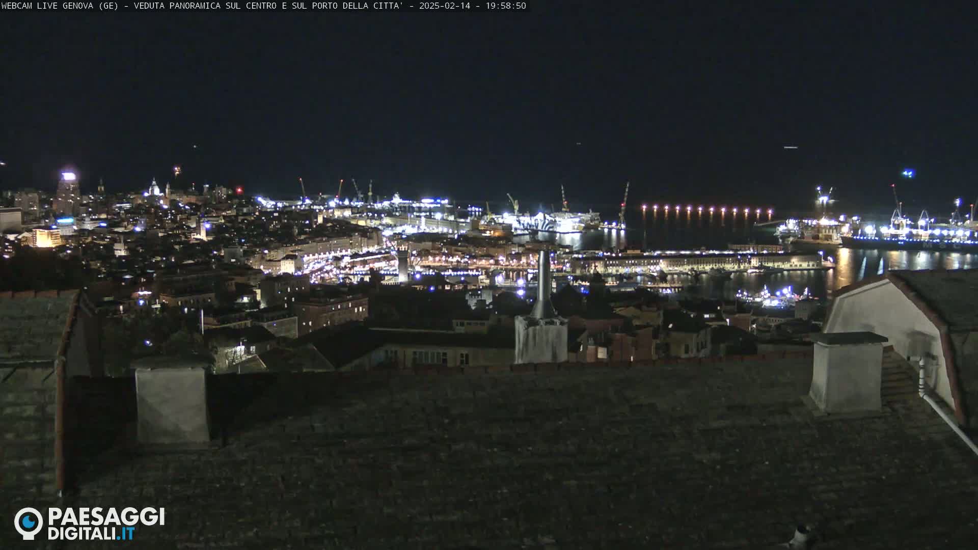 A nighttime, panoramic view of a city's harbor and cityscape, illuminated with lights.