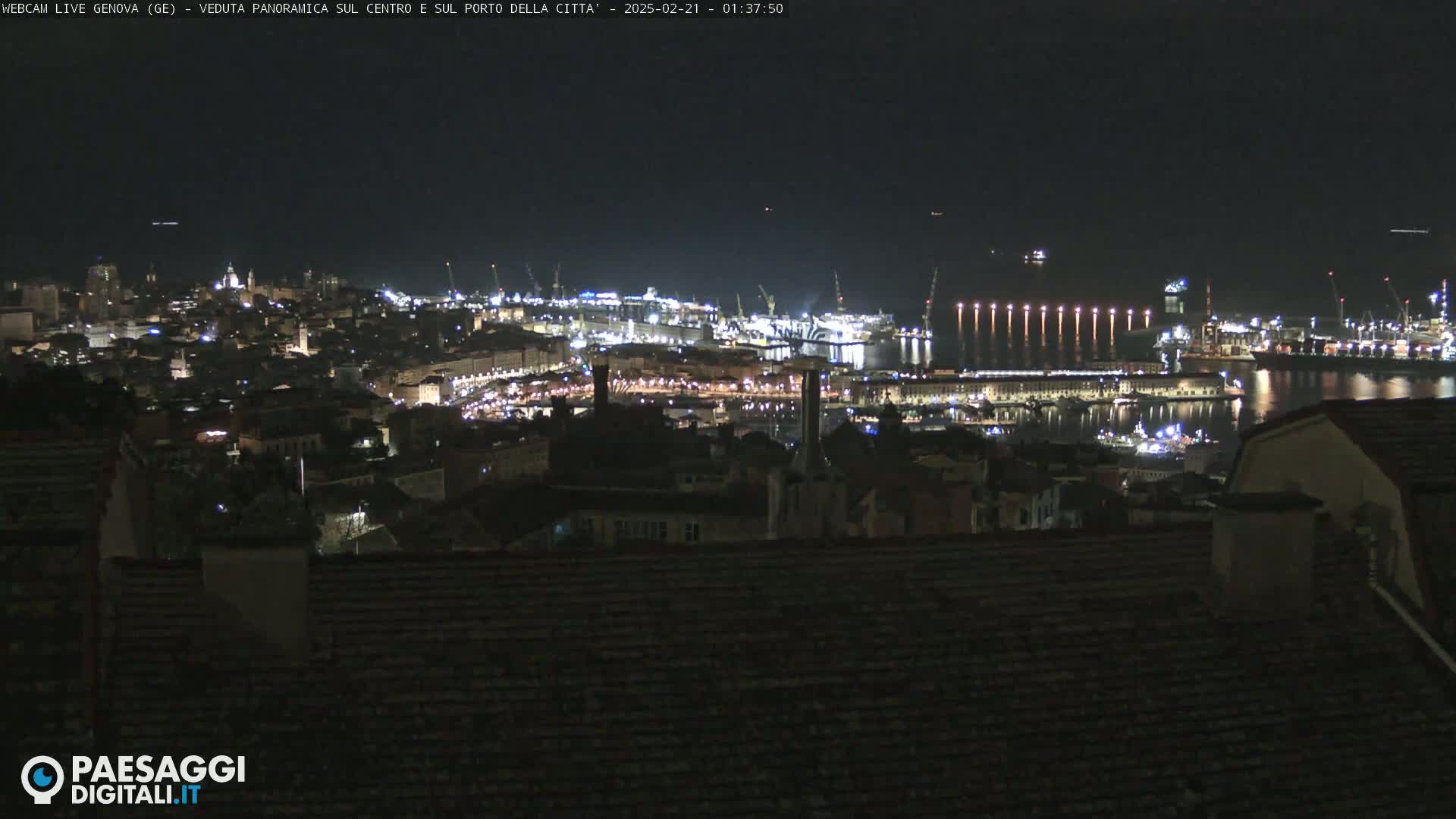 A nighttime panoramic view of a city and its harbor, illuminated by many lights, under a clear, dark sky.