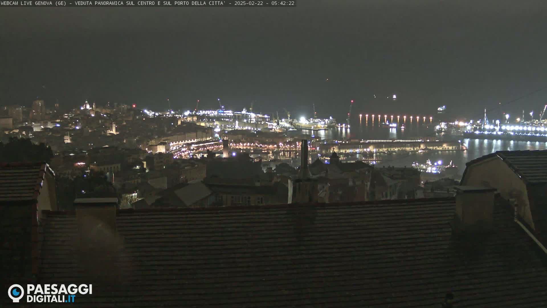 A nighttime panoramic view of a city's harbor and illuminated buildings, under a dark, possibly overcast sky.