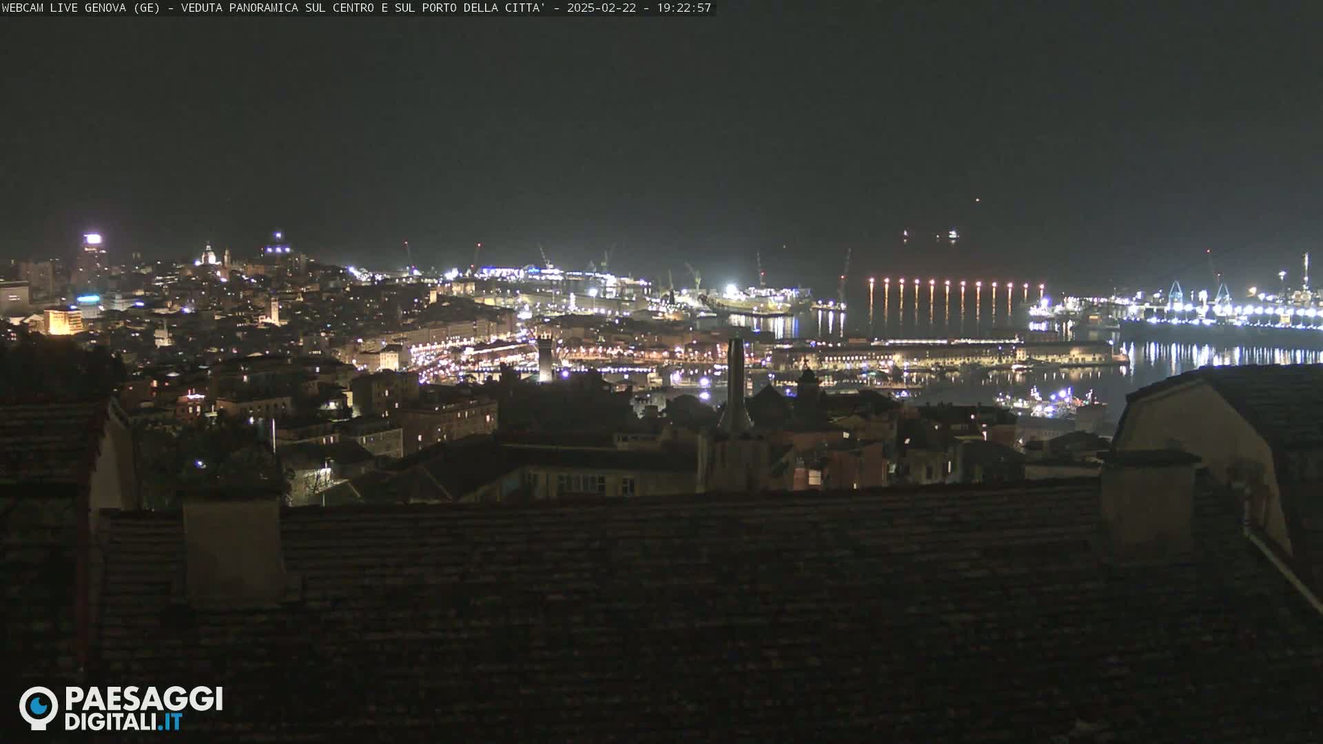 A nighttime panoramic view of a city and harbor, brightly lit against a dark sky.