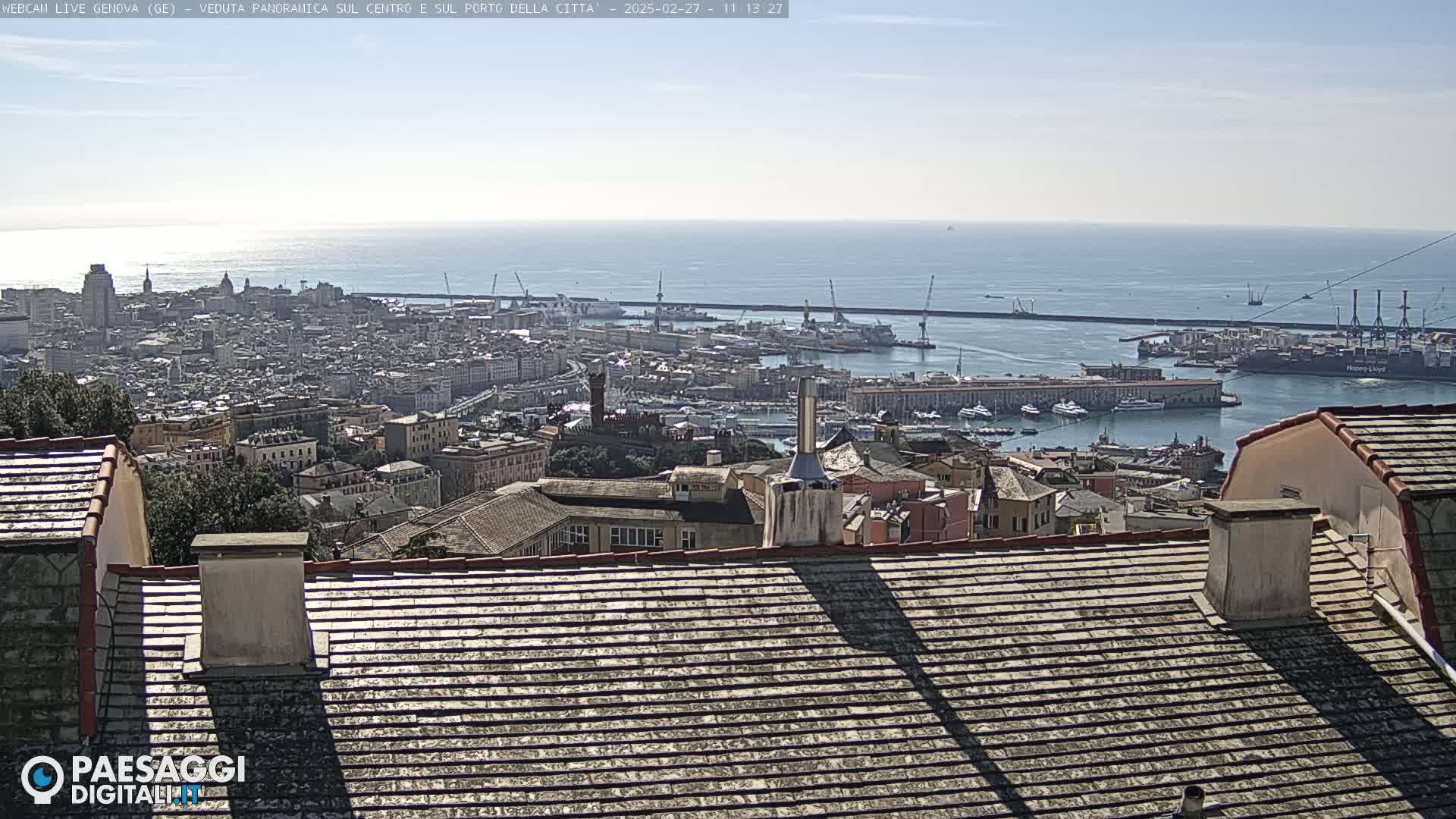 A panoramic view of a city harbor and cityscape on a clear, sunny day, seen from a rooftop overlooking the ocean.