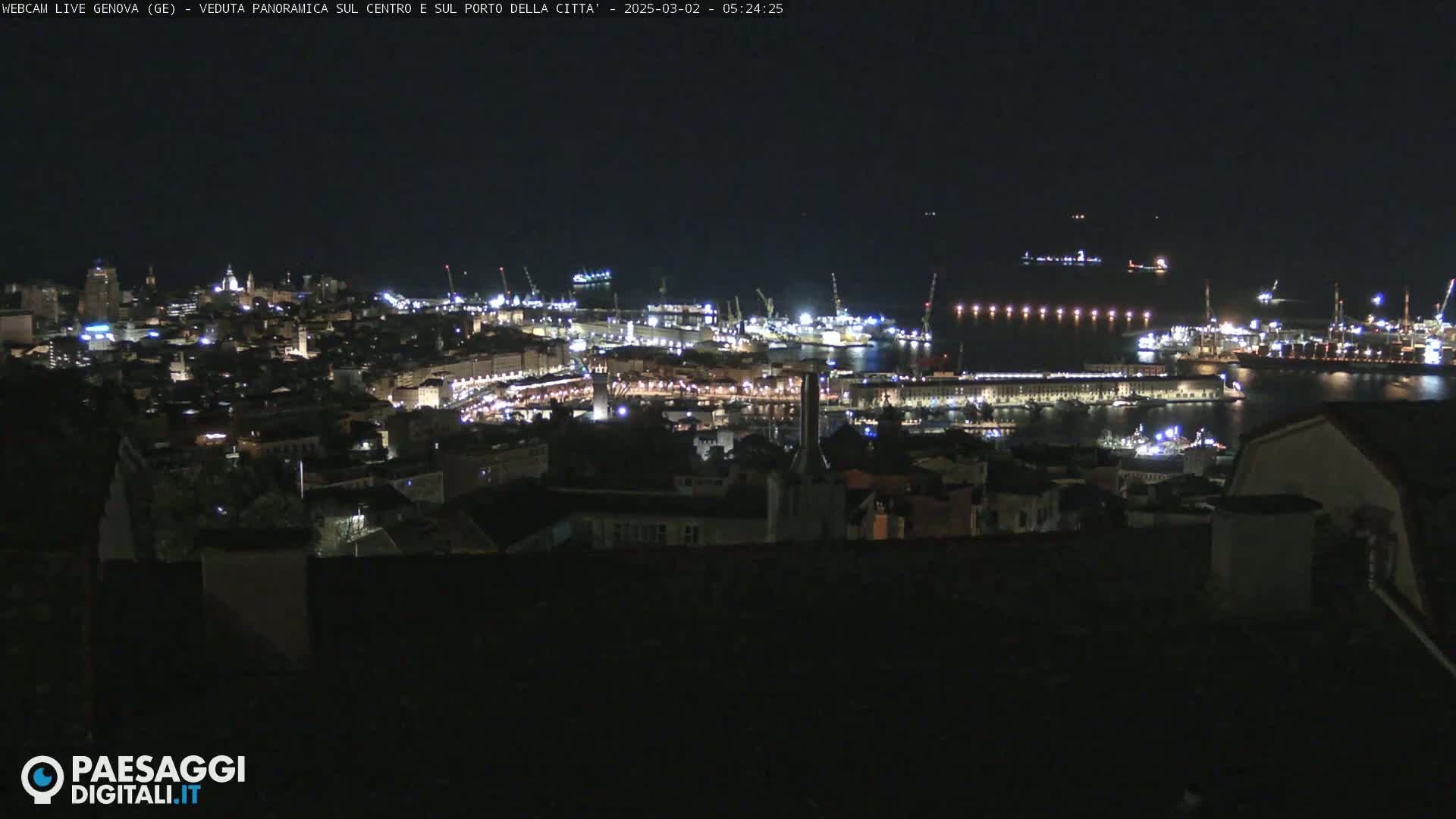 A nighttime panoramic view of a city's harbor and buildings, illuminated with many lights.