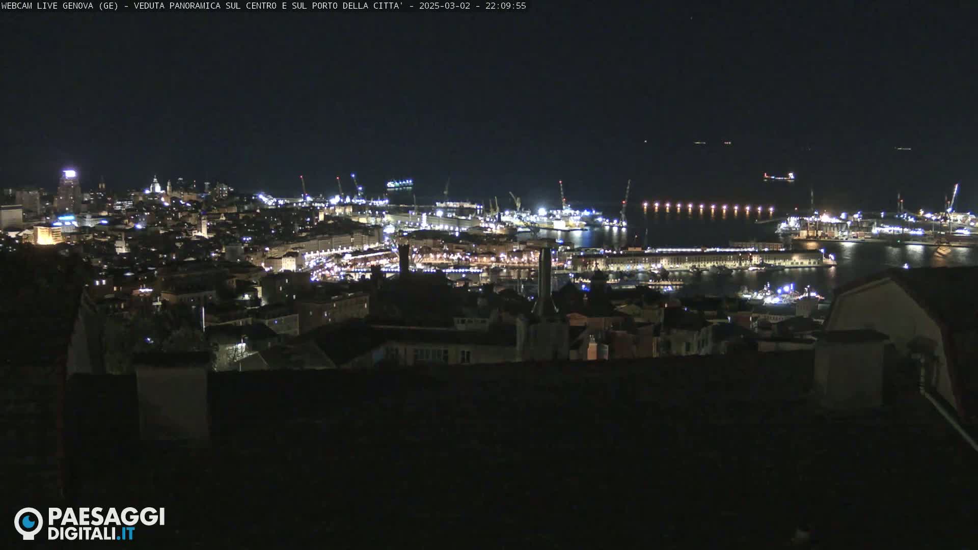 A nighttime panoramic view of a city's harbor and illuminated buildings, under a clear, dark sky.