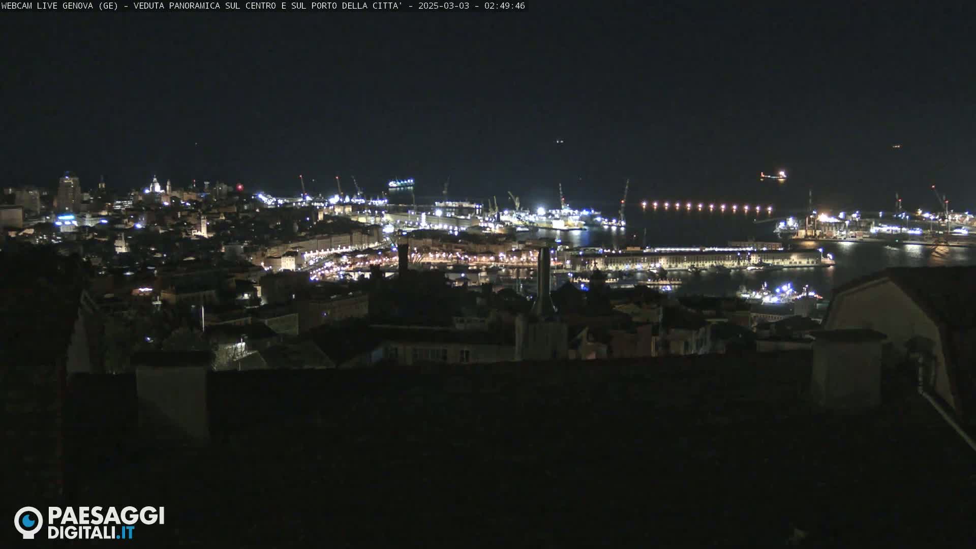 A nighttime panoramic view of a city's harbor and illuminated buildings.