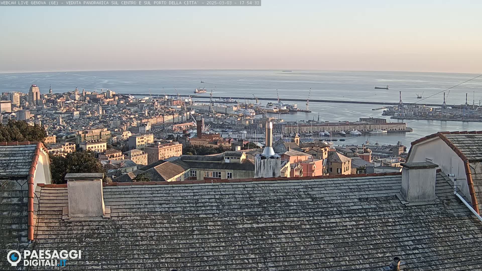 A panoramic view of a city and harbor on a calm, sunlit day, with the ocean in the background.