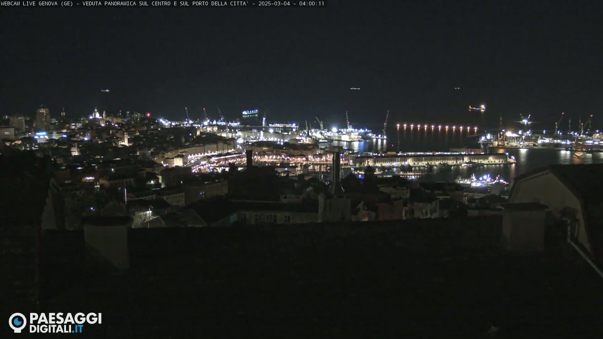A nighttime, panoramic view of a city's illuminated harbor and buildings.