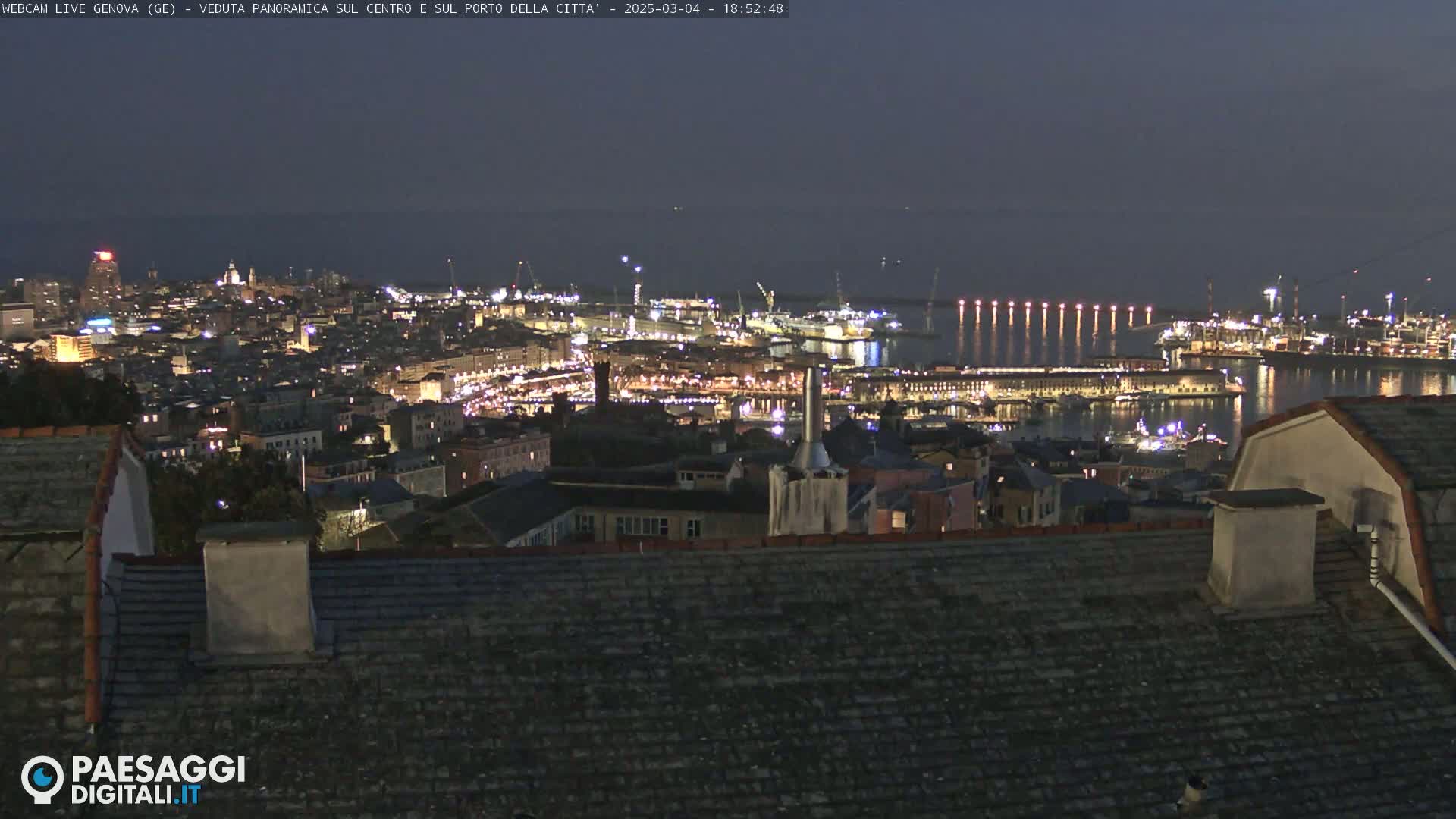A nighttime panoramic view of a city's illuminated harbor and buildings, with calm waters under a dark sky.