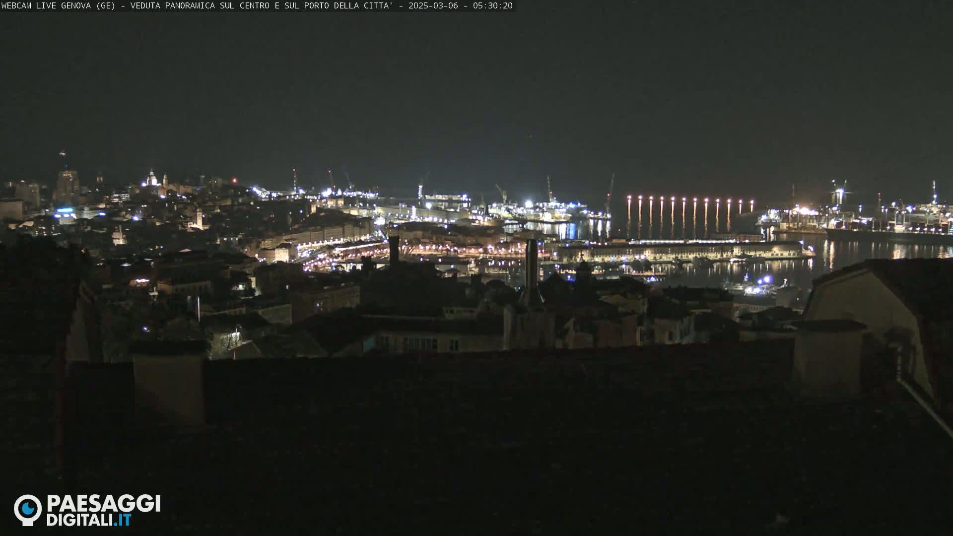 A nighttime, panoramic view of a city's illuminated harbor and buildings.