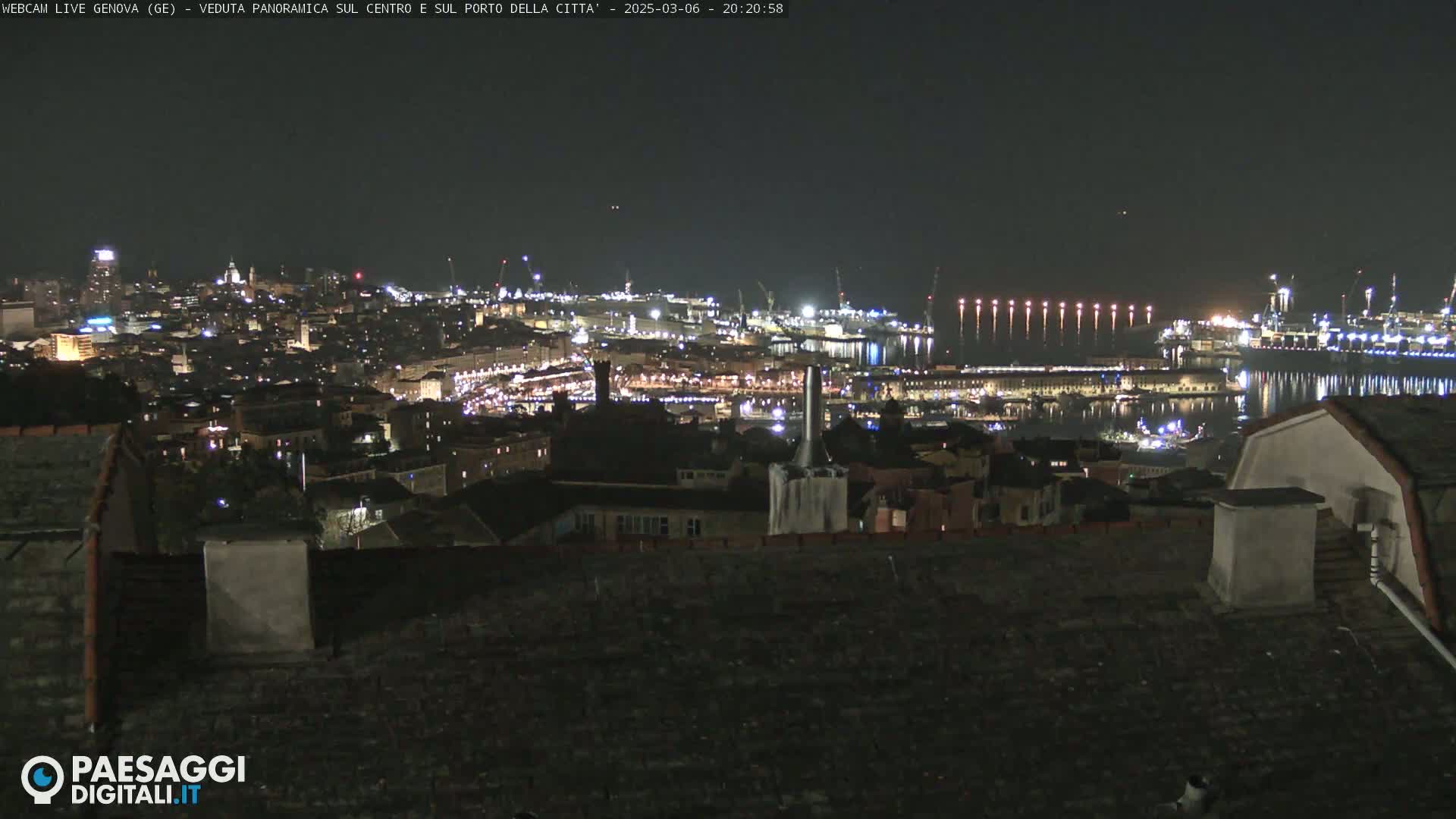 A nighttime panoramic view of a city harbor illuminated with lights, under a clear dark sky.