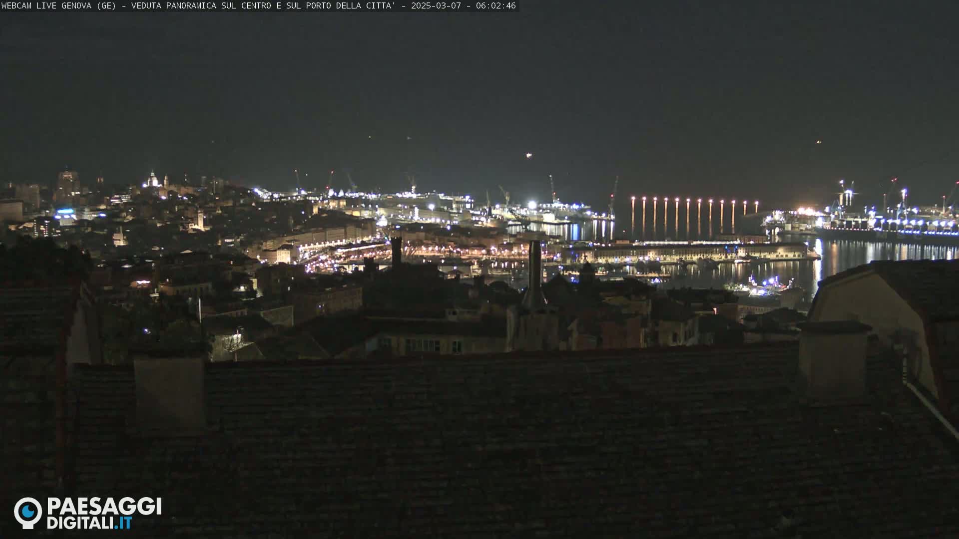 A nighttime, panoramic view of a city's harbor and illuminated cityscape.