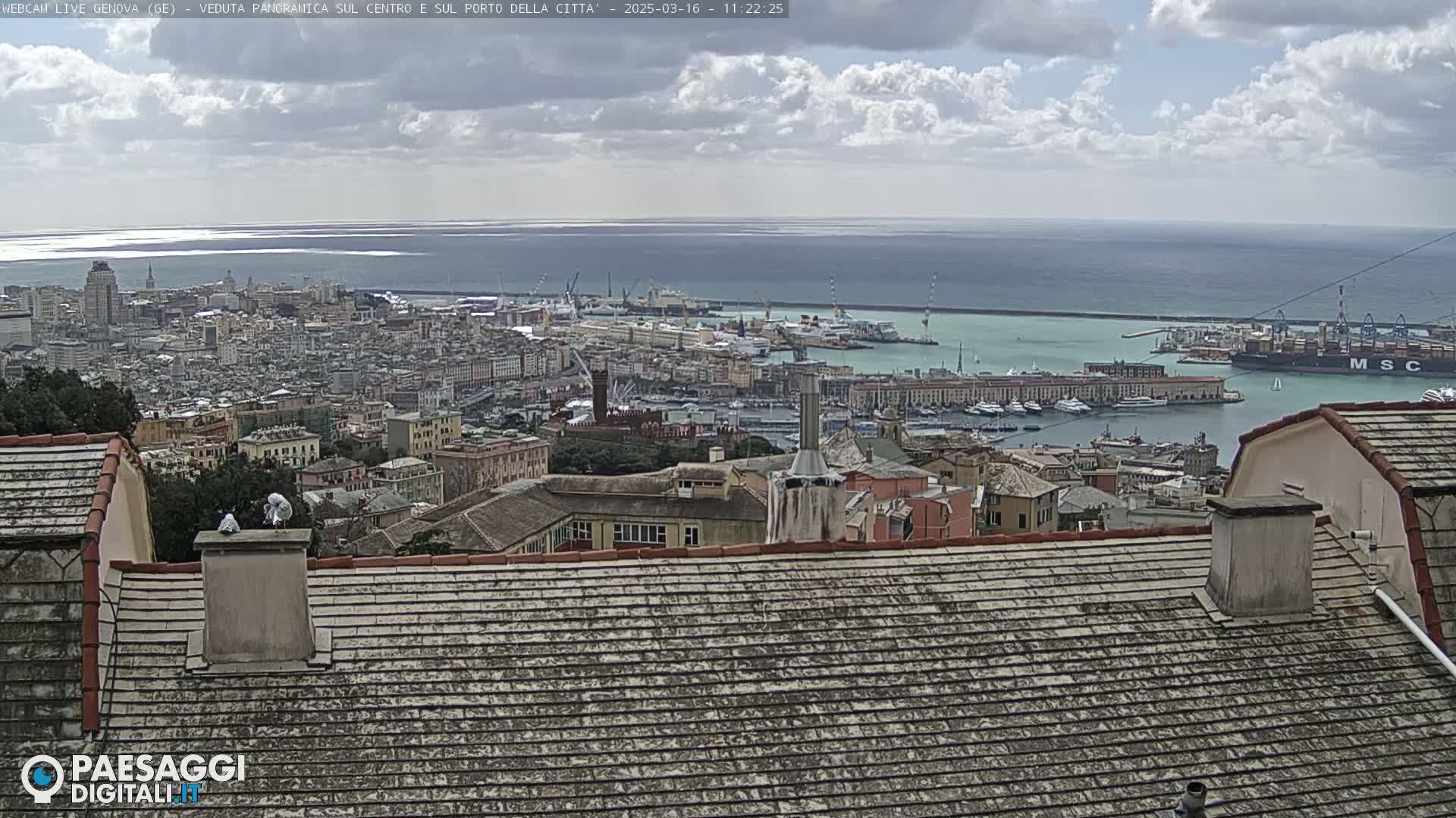 A partly cloudy day overlooks a city's harbor filled with boats and ships, extending to a calm ocean.