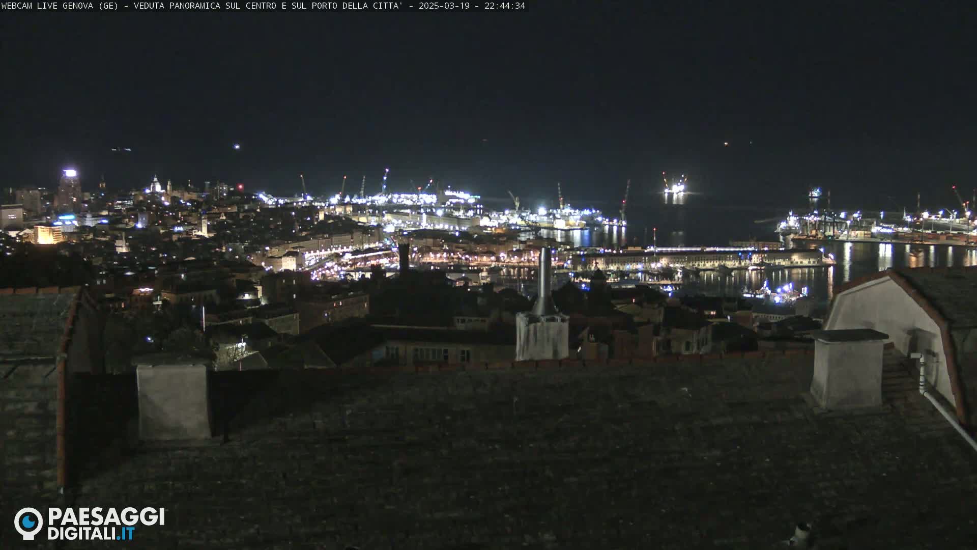 A nighttime, panoramic view of a city harbor with many lights illuminating buildings and ships.