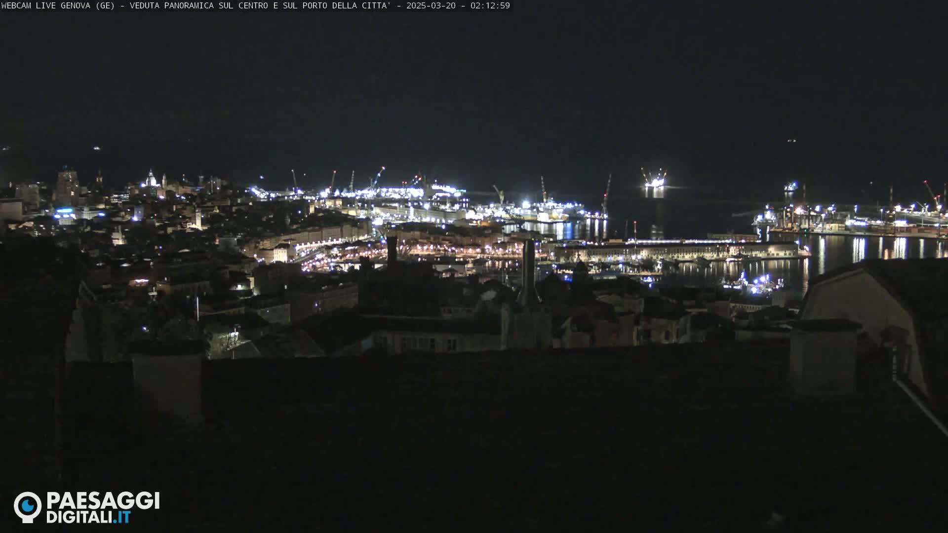 A nighttime, panoramic view of a city's harbor and illuminated cityscape, with calm water reflecting the lights.
