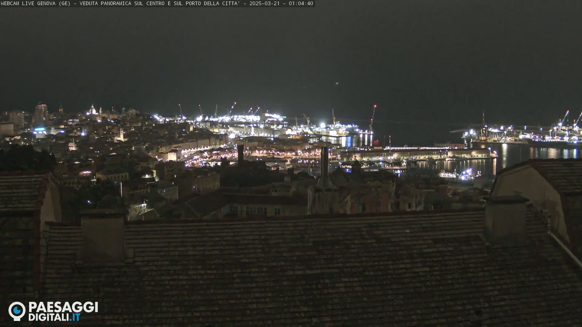 A nighttime panoramic view of a city's illuminated harbor and buildings, under a dark sky.