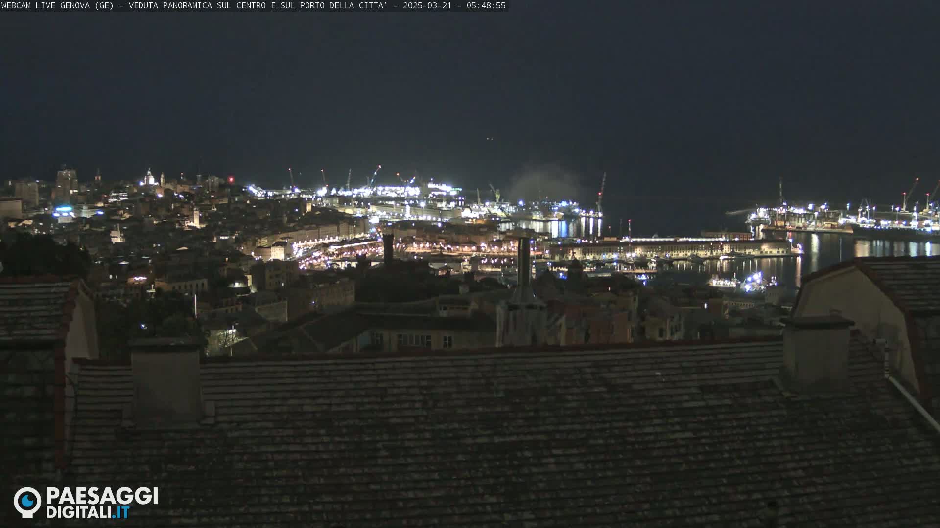 A nighttime, panoramic view of a city's illuminated harbor and buildings, with a dark sky.