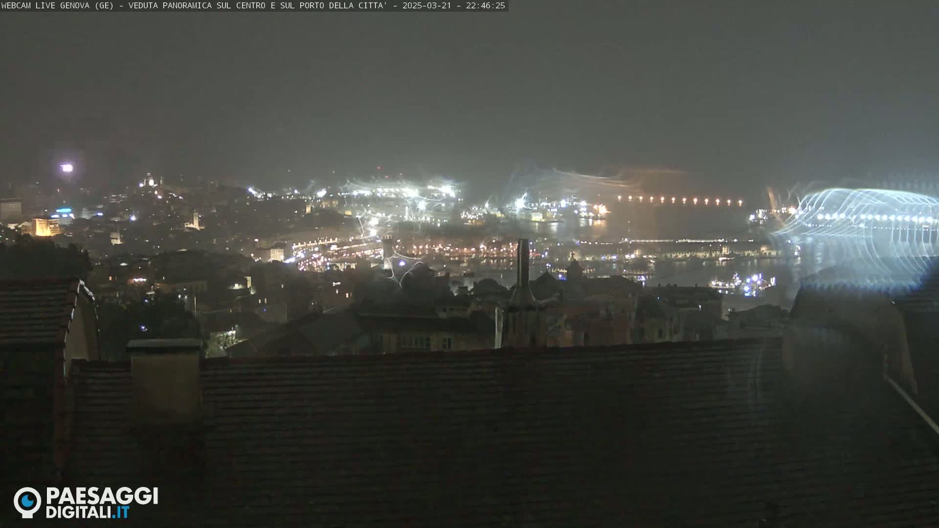 A nighttime view of a city and harbor illuminated by lights, with some rain or light snow visible in the air.