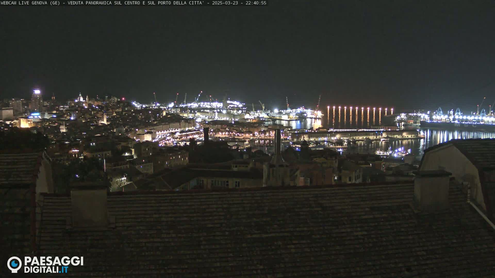 A nighttime panoramic view of a city's illuminated harbor and buildings, under a clear, dark sky.