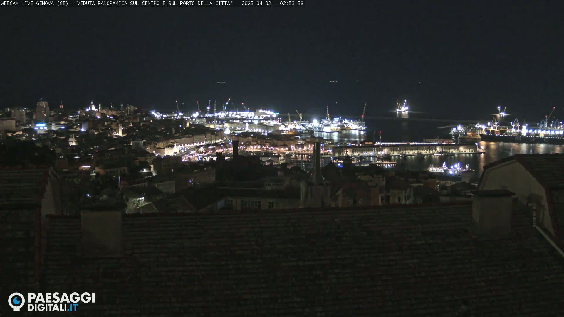 A nighttime, panoramic view of a city's harbor and illuminated cityscape.