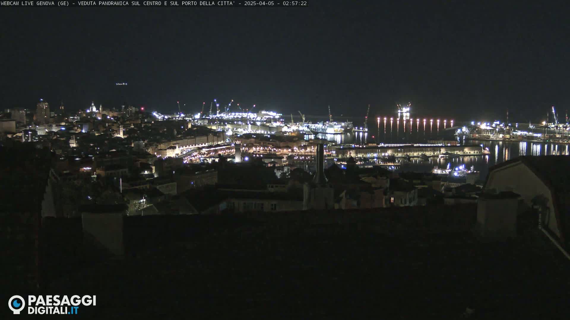 A nighttime, panoramic view of a city and its harbor, brightly lit, under a clear, dark sky.