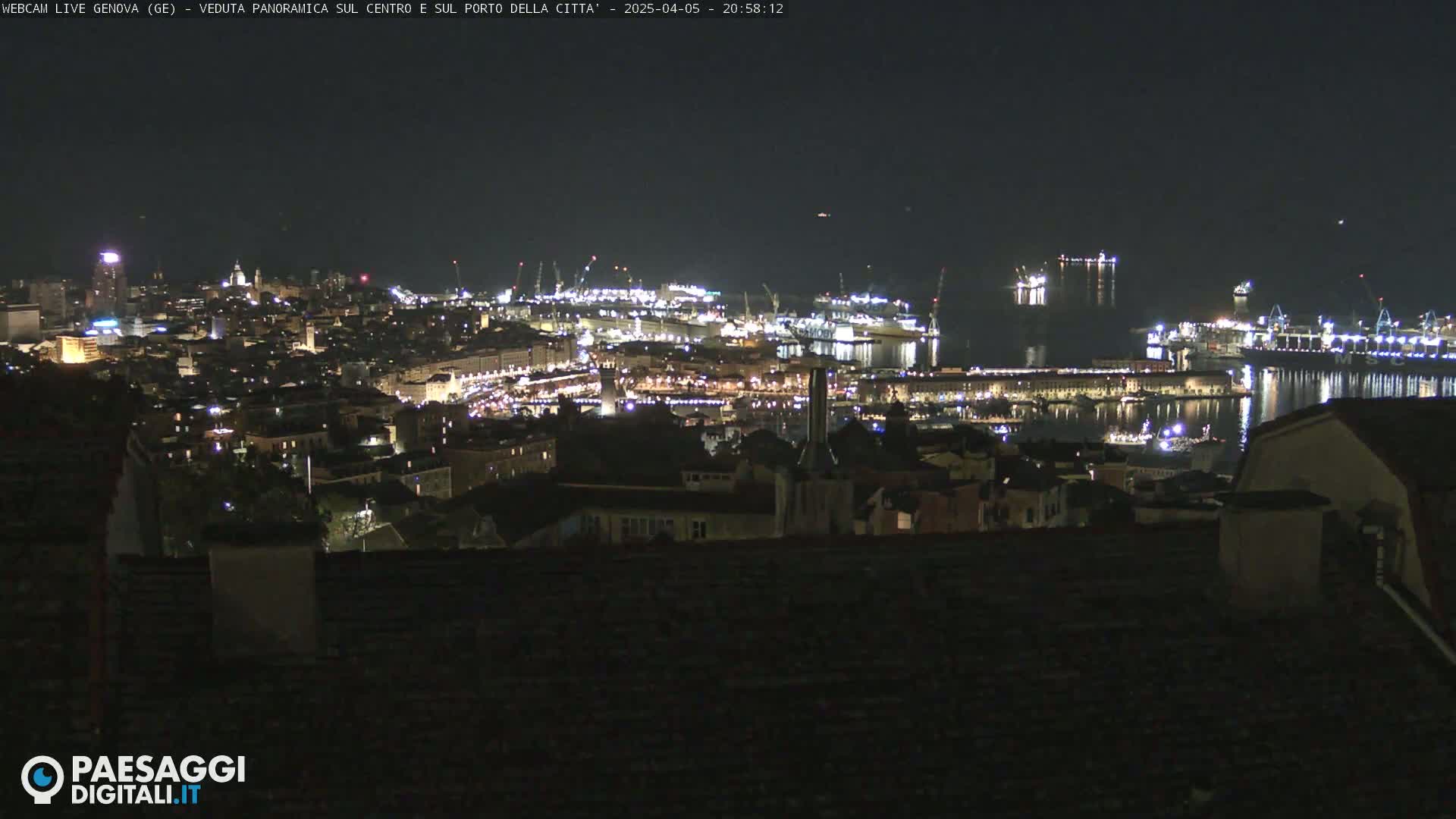 A nighttime panoramic view of a city's illuminated harbor and buildings, with calm water reflecting the city lights.