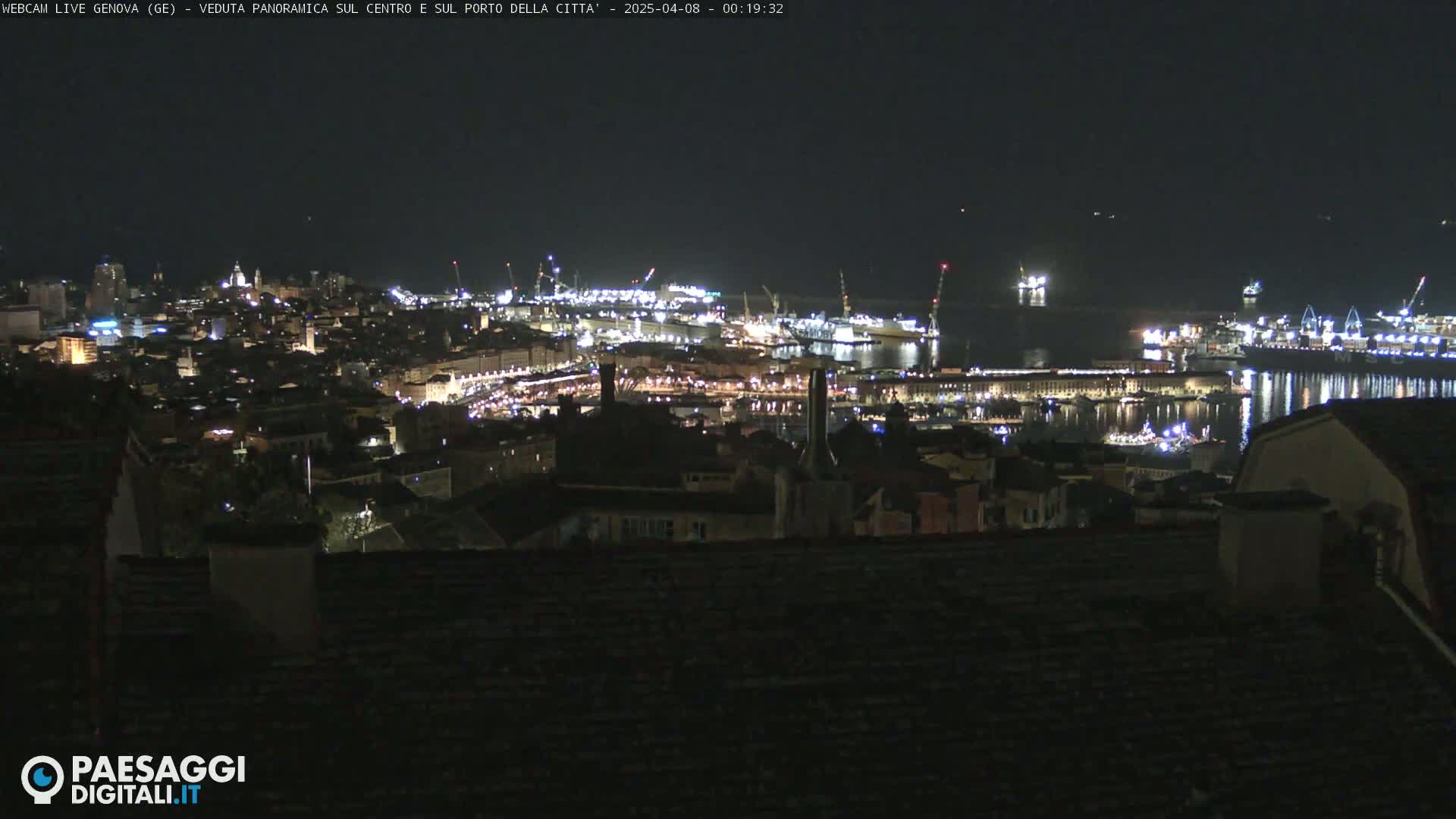 A nighttime panoramic view of a city's illuminated harbor and buildings, with a dark sky.