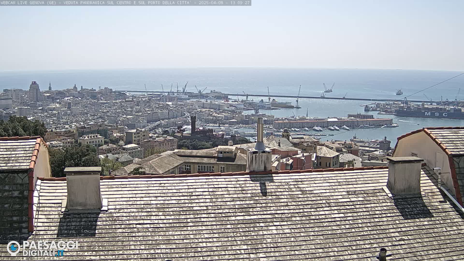 A panoramic view of a city and harbor on a sunny day, with the city extending to a large body of water in the distance.