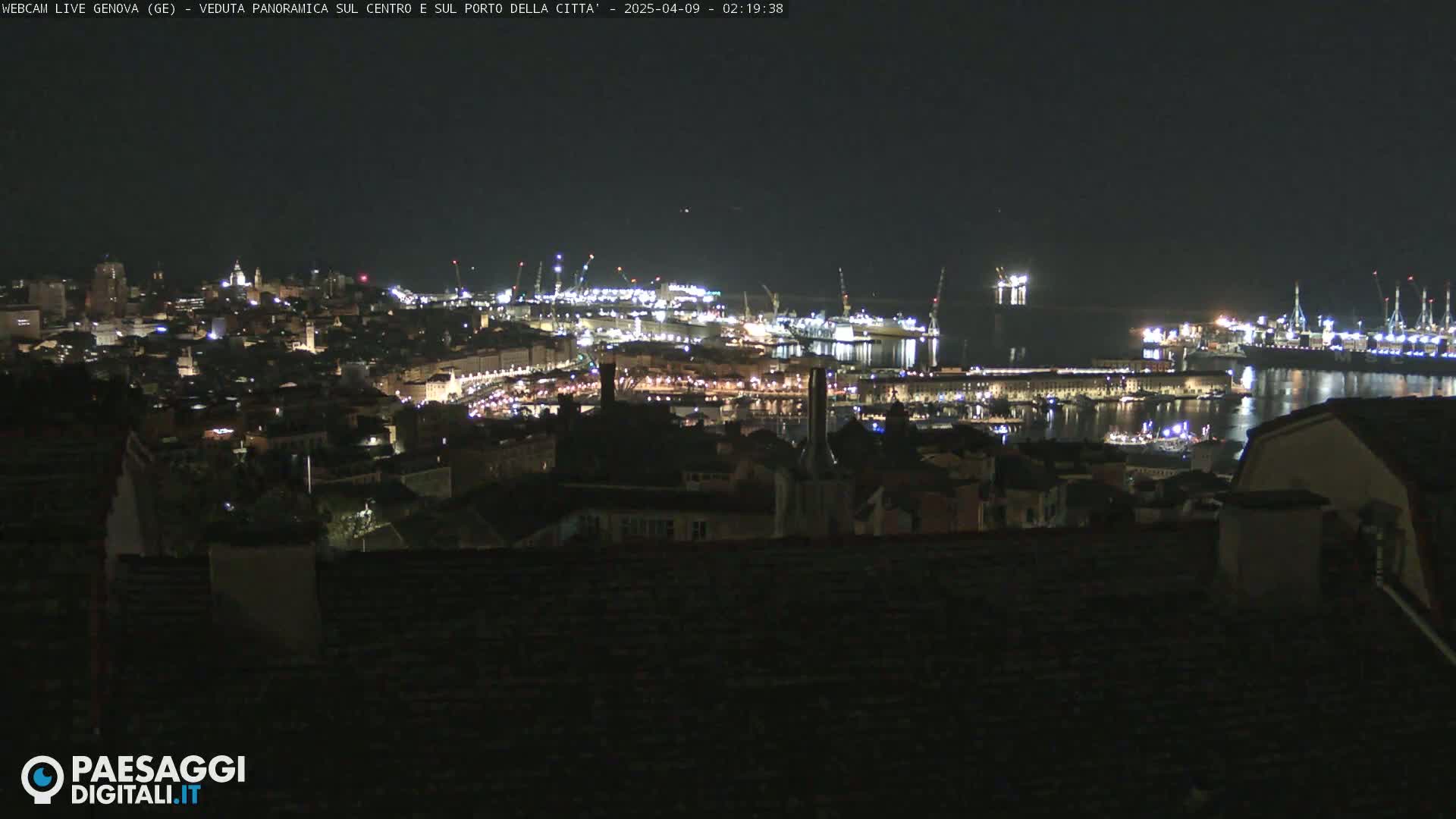 A nighttime, panoramic view of a city and harbor illuminated by lights, under a clear, dark sky.