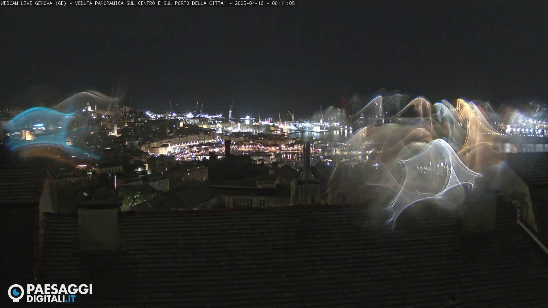 A nighttime, panoramic view of a brightly lit city and harbor, overlaid with streaks of light, possibly from a light show or camera artifact.
