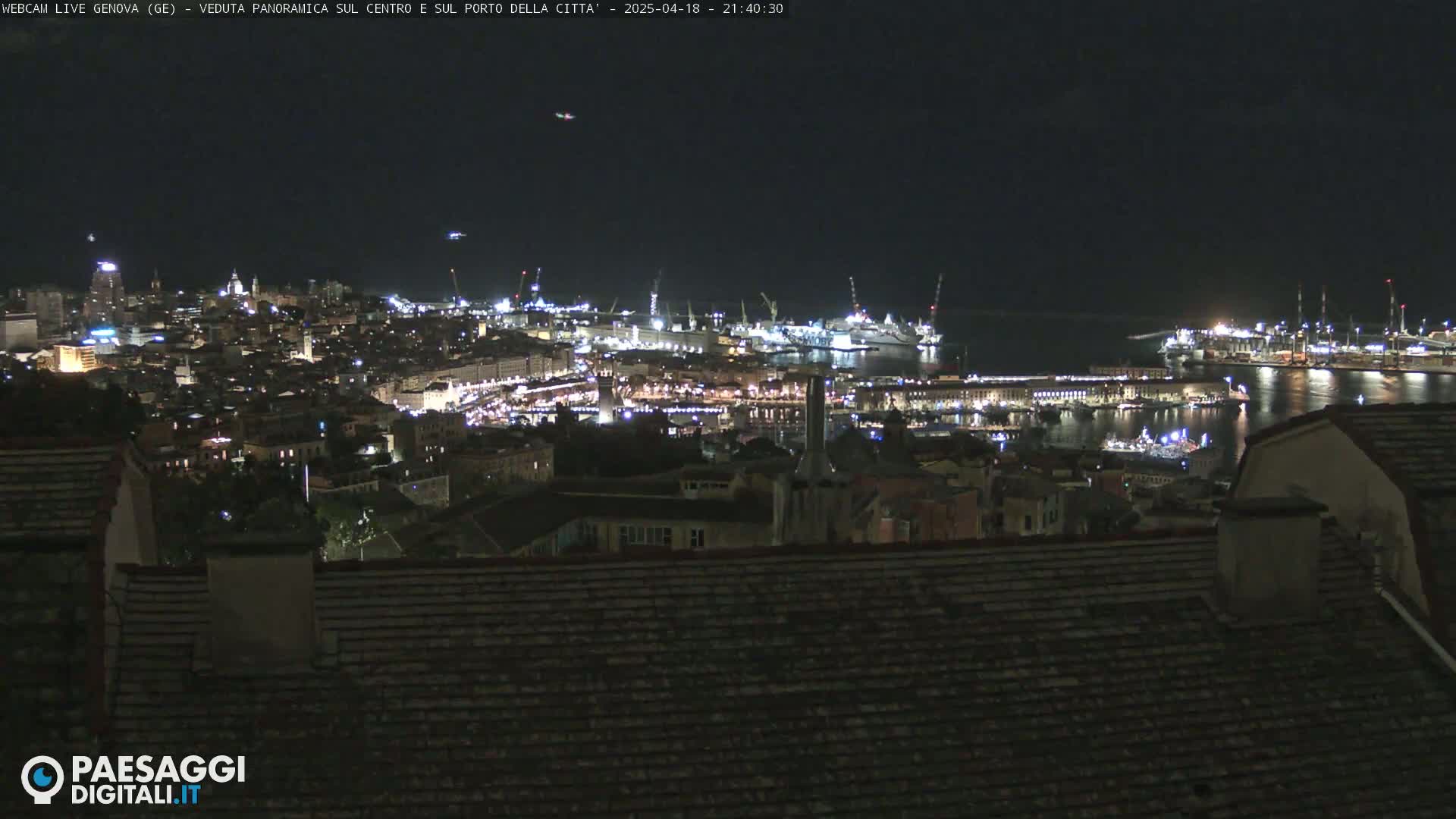 A nighttime, panoramic view of a city's harbor and illuminated cityscape, seen from a rooftop.